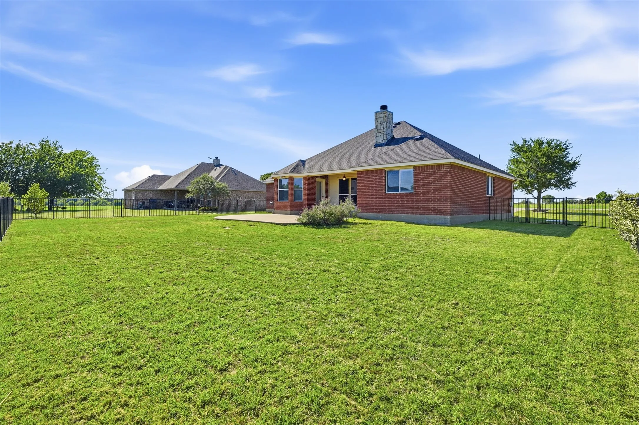 Expansive back yard featuring a large concrete patio, covered porch and iron fencing.