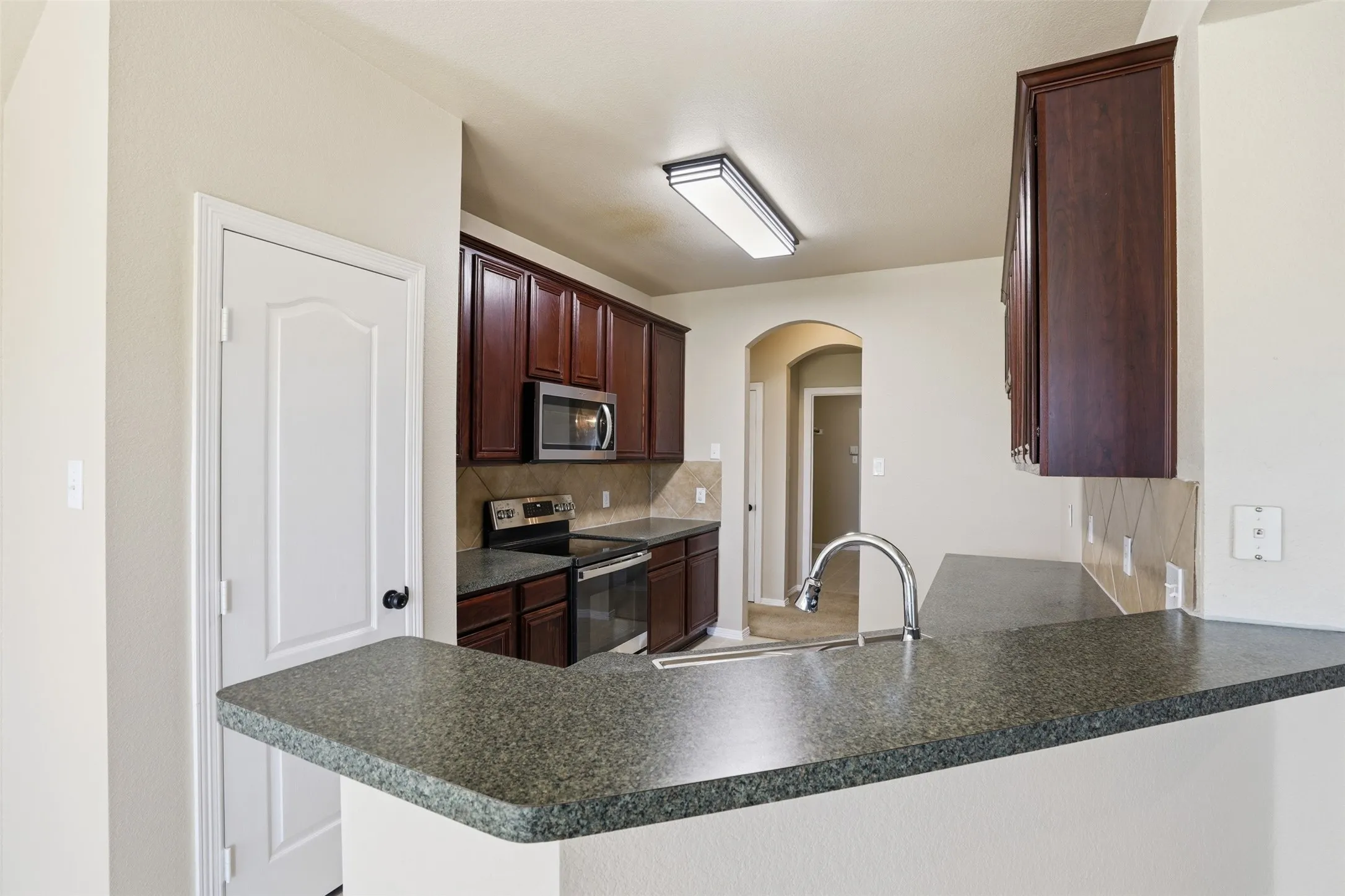 Kitchen featuring dark wood cabinetry, stainless steel microwave, range and sink.