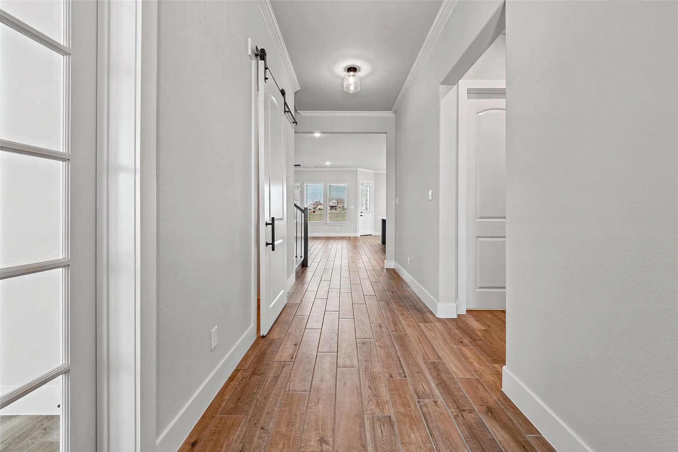 Wood-finish plank flooring throughout, white interior walls, crown molding, and a barn door with matte black hardware