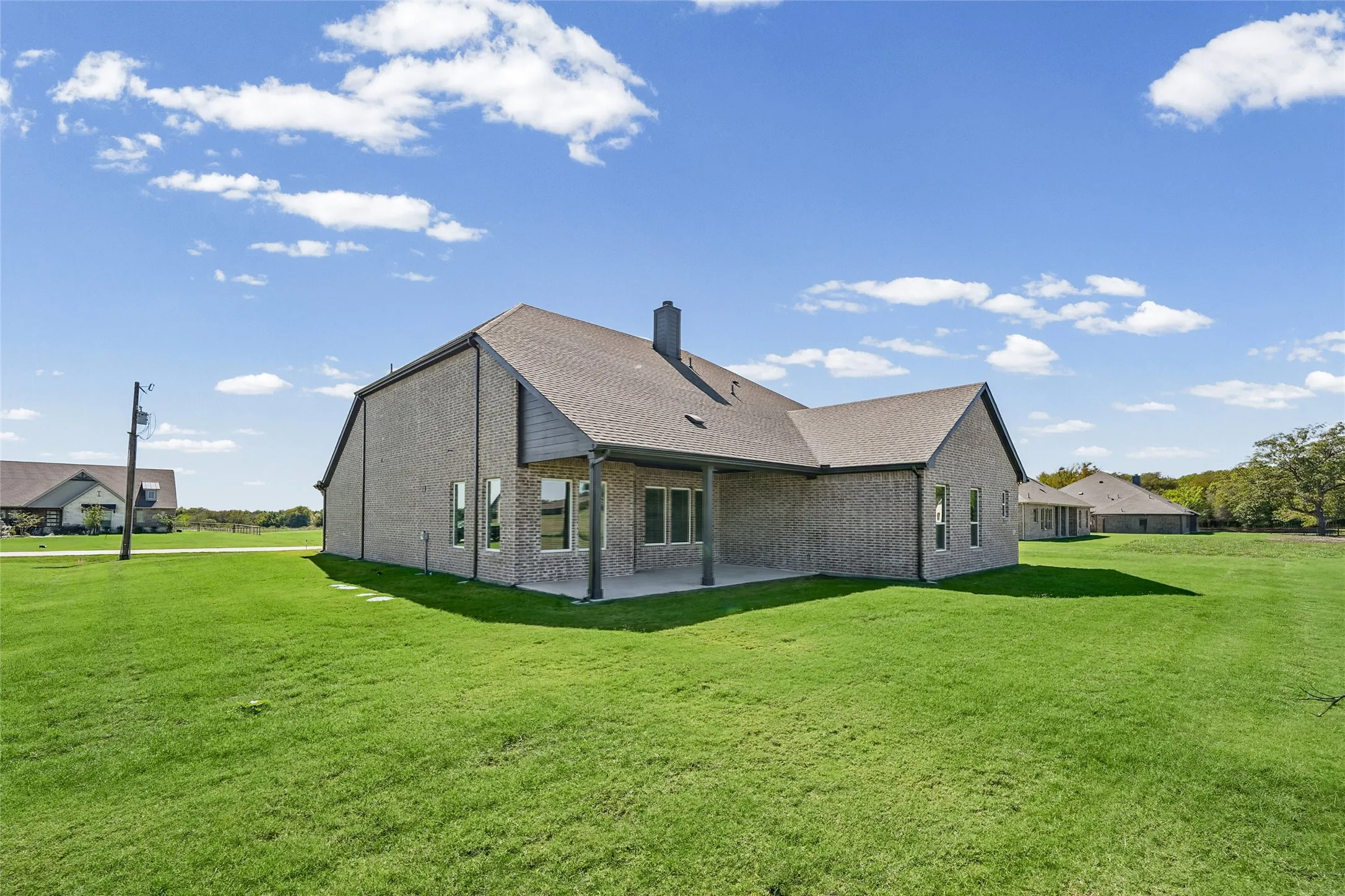 Expansive green lawn surrounds a brick exterior home with a covered patio