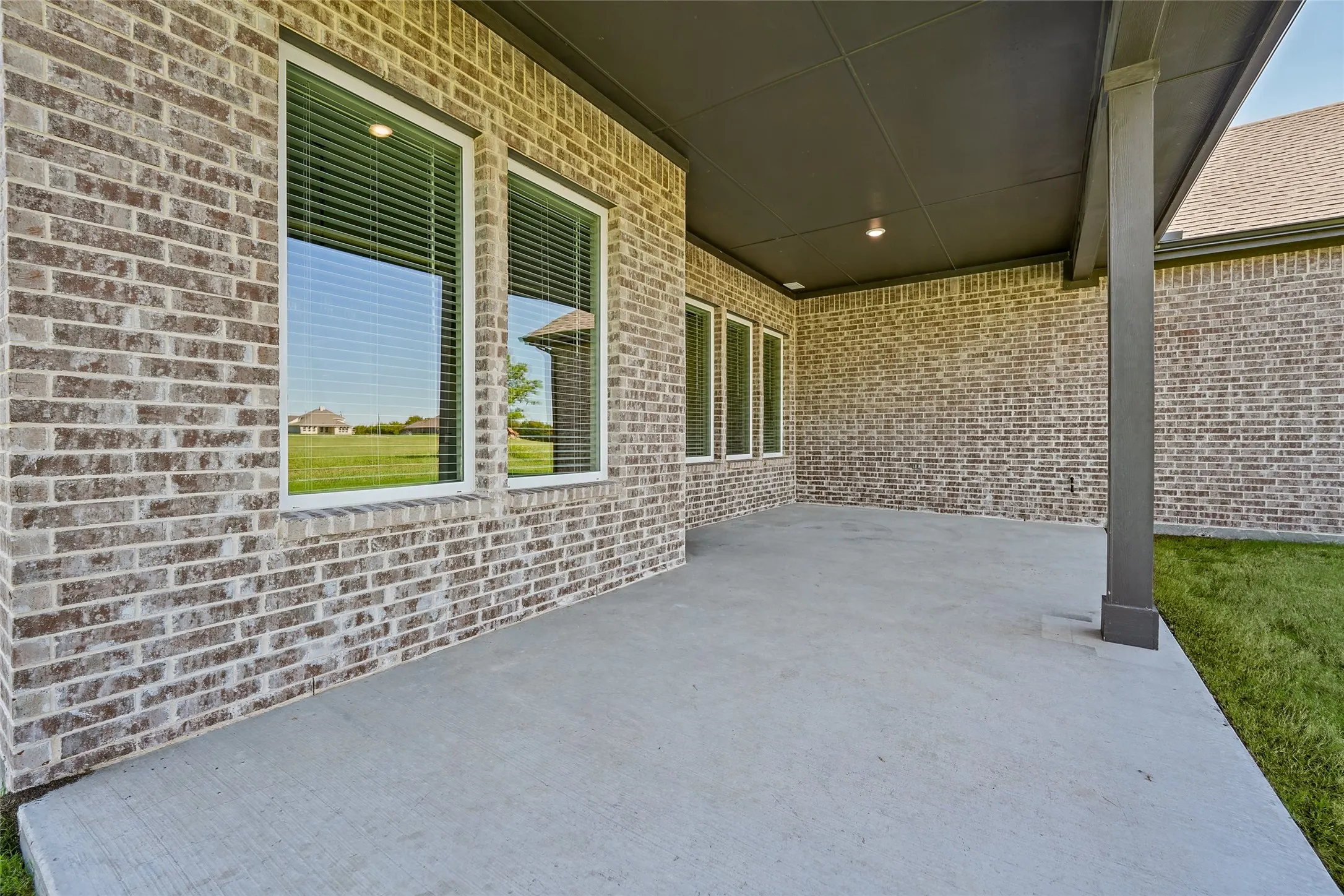 Covered patio featuring a concrete surface, brick exterior, support columns, and recessed lighting