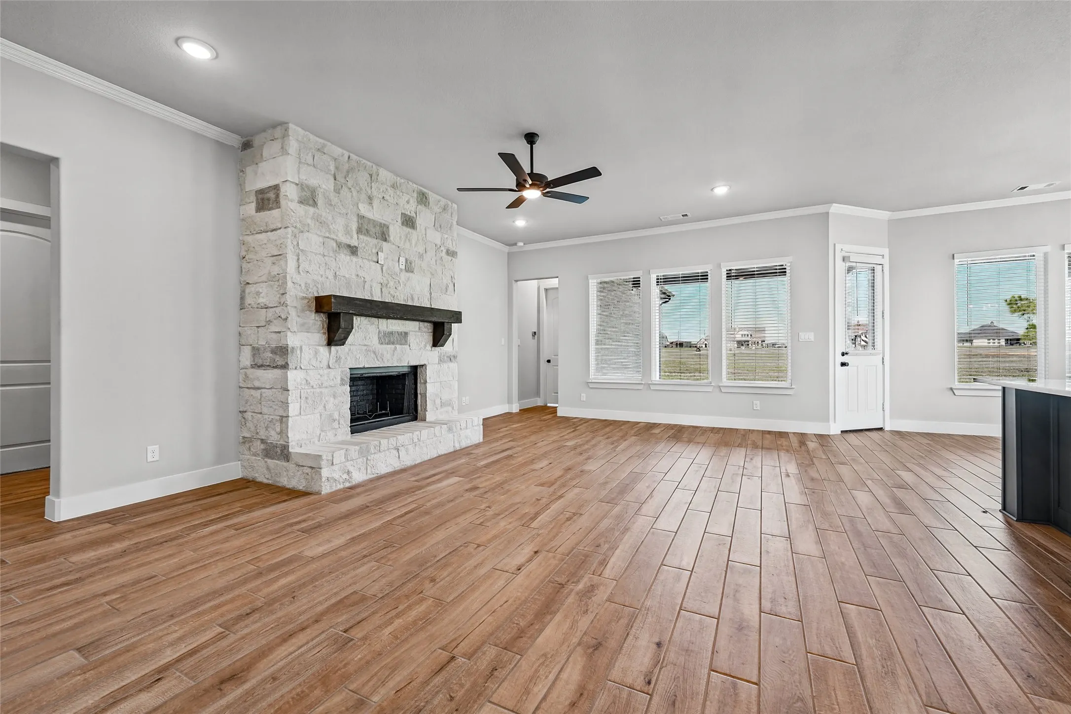 Stone-clad fireplace with a wood-finish mantel, wood-finish flooring, recessed lighting, ceiling fan, and multiple windows