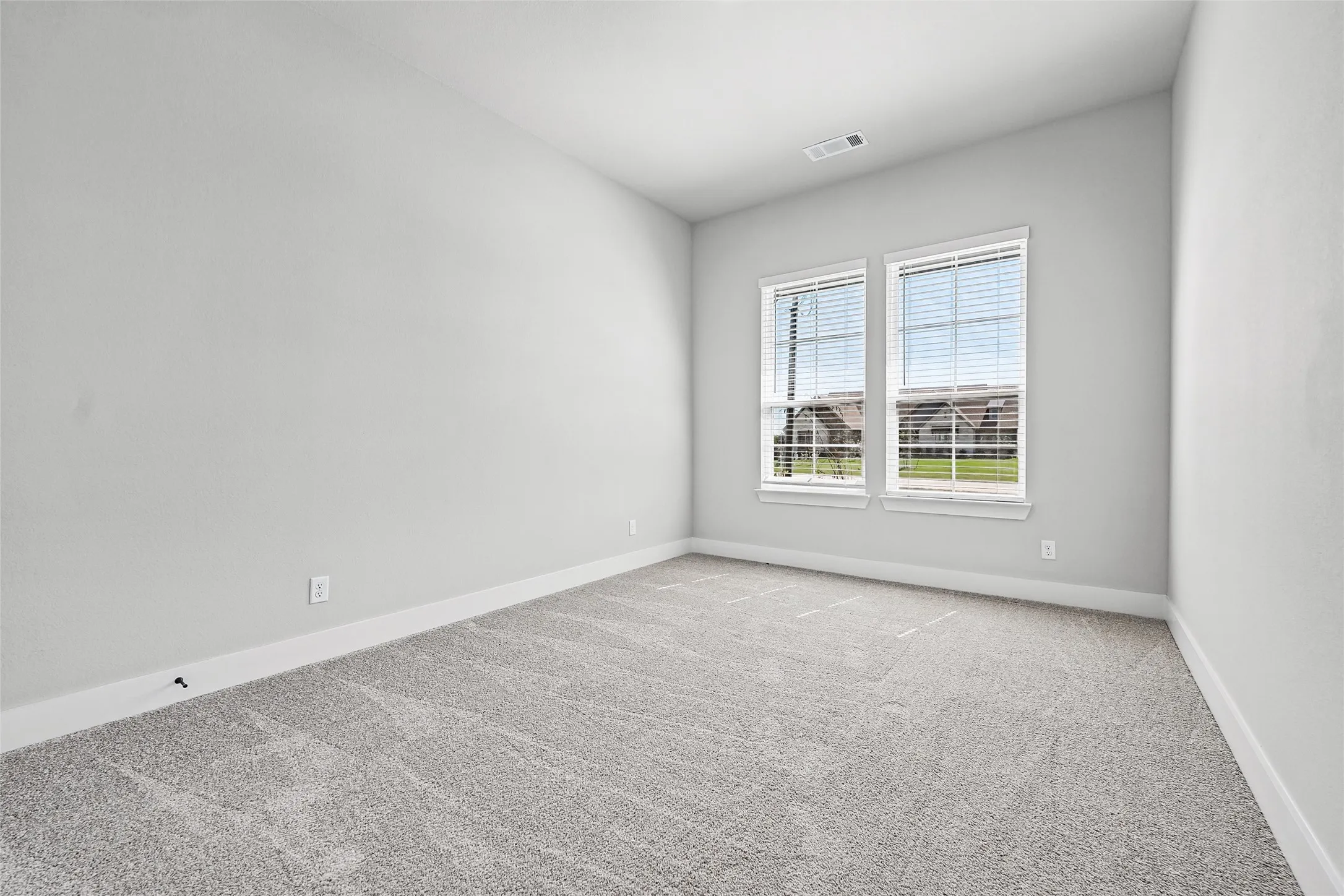 Neutral gray wall color, textured carpeting, two windows with blinds, white trim, and a ceiling-mounted register