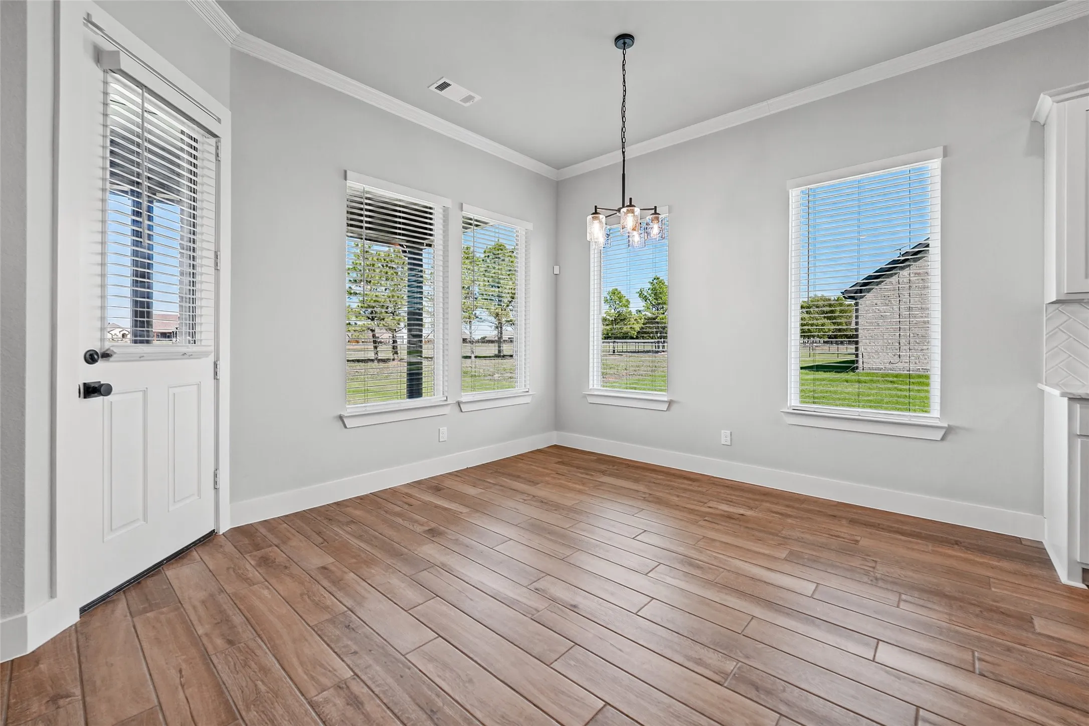 Wood-finish plank flooring, multiple windows with blinds, crown molding, and a contemporary chandelier