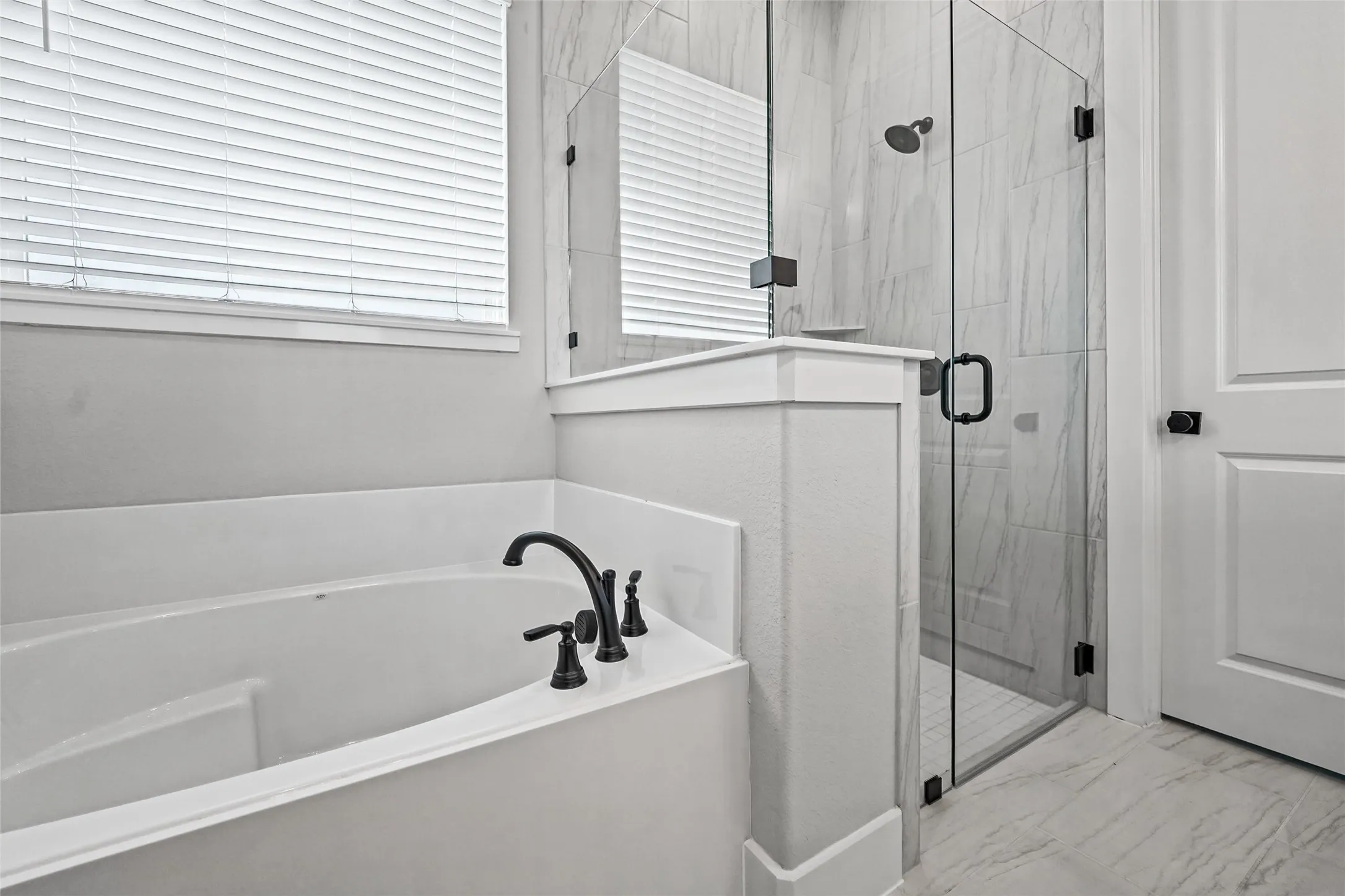 Soaking tub with matte black fixtures, adjacent to a frameless glass shower enclosure featuring tiled walls, and a white paneled door with a black knob