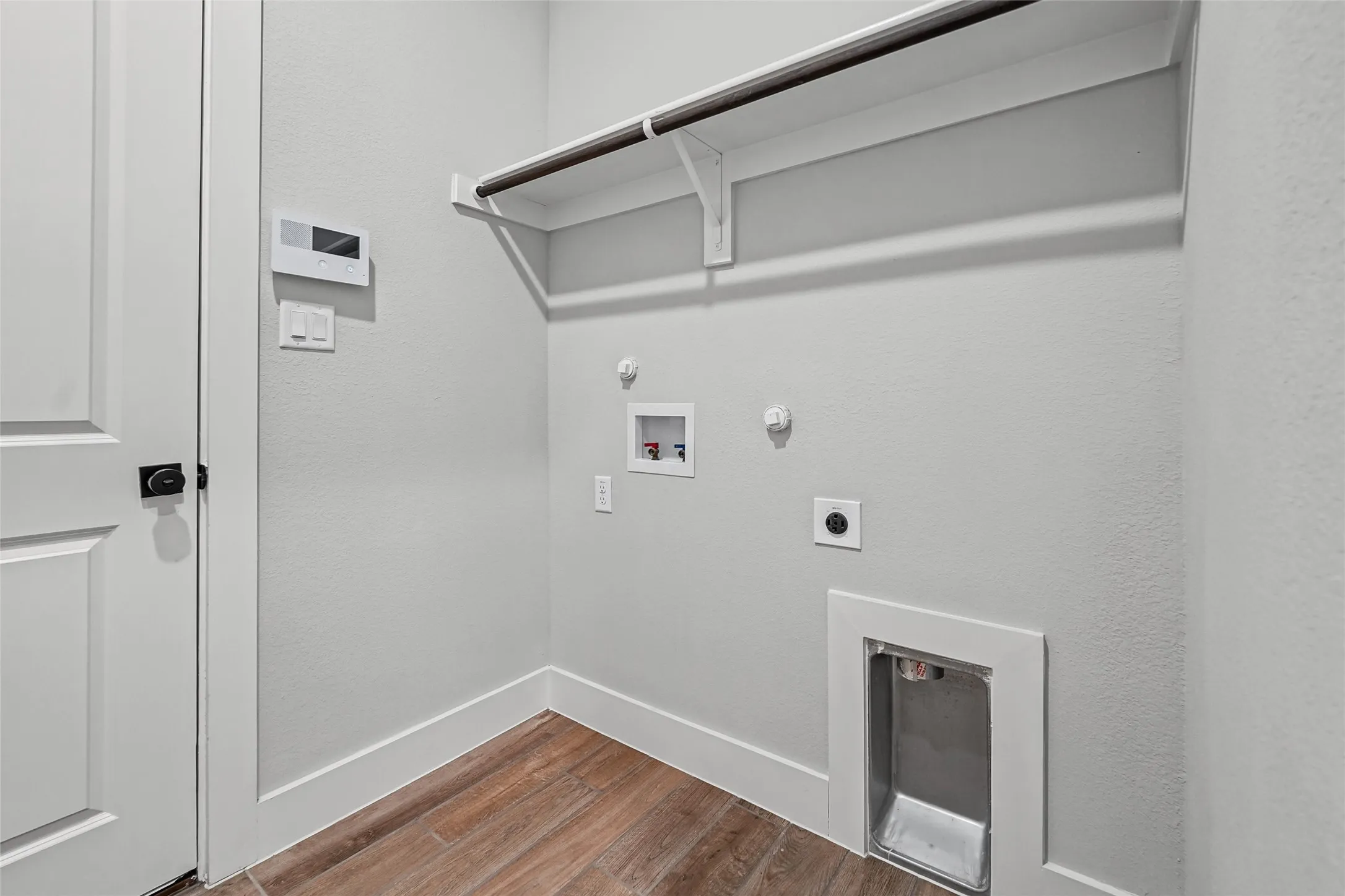 Wood-finish flooring with white baseboards, a wall-mounted clothing rod, and an integrated utility sink