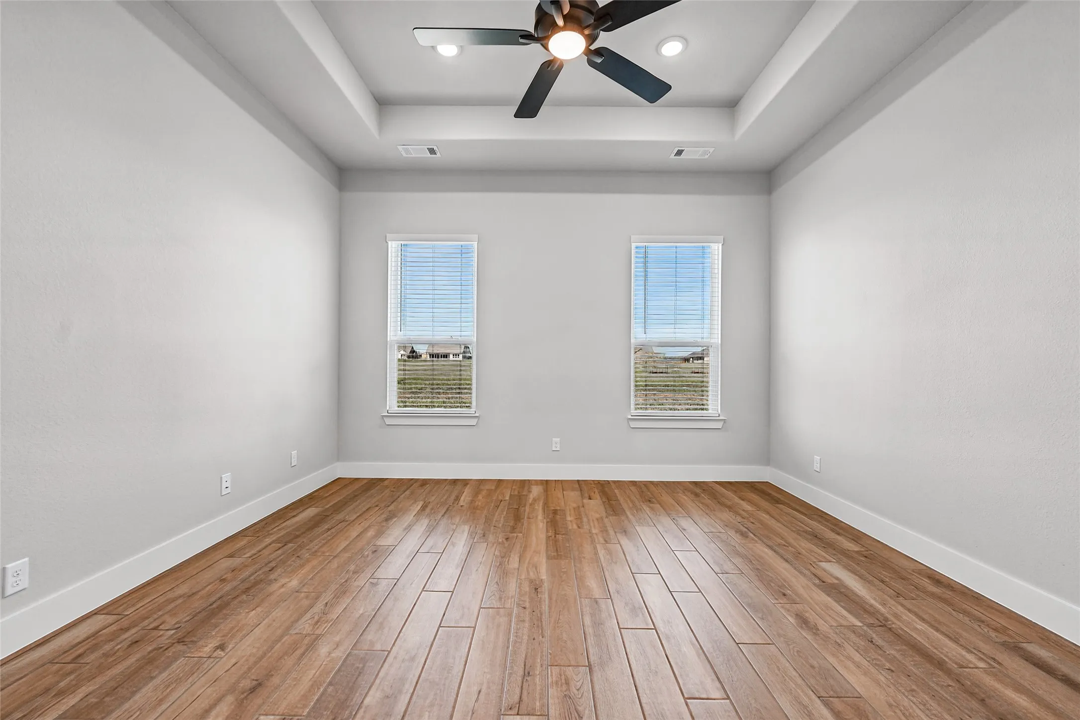 Tray ceiling with recessed lighting, wood-finish flooring, and two windows