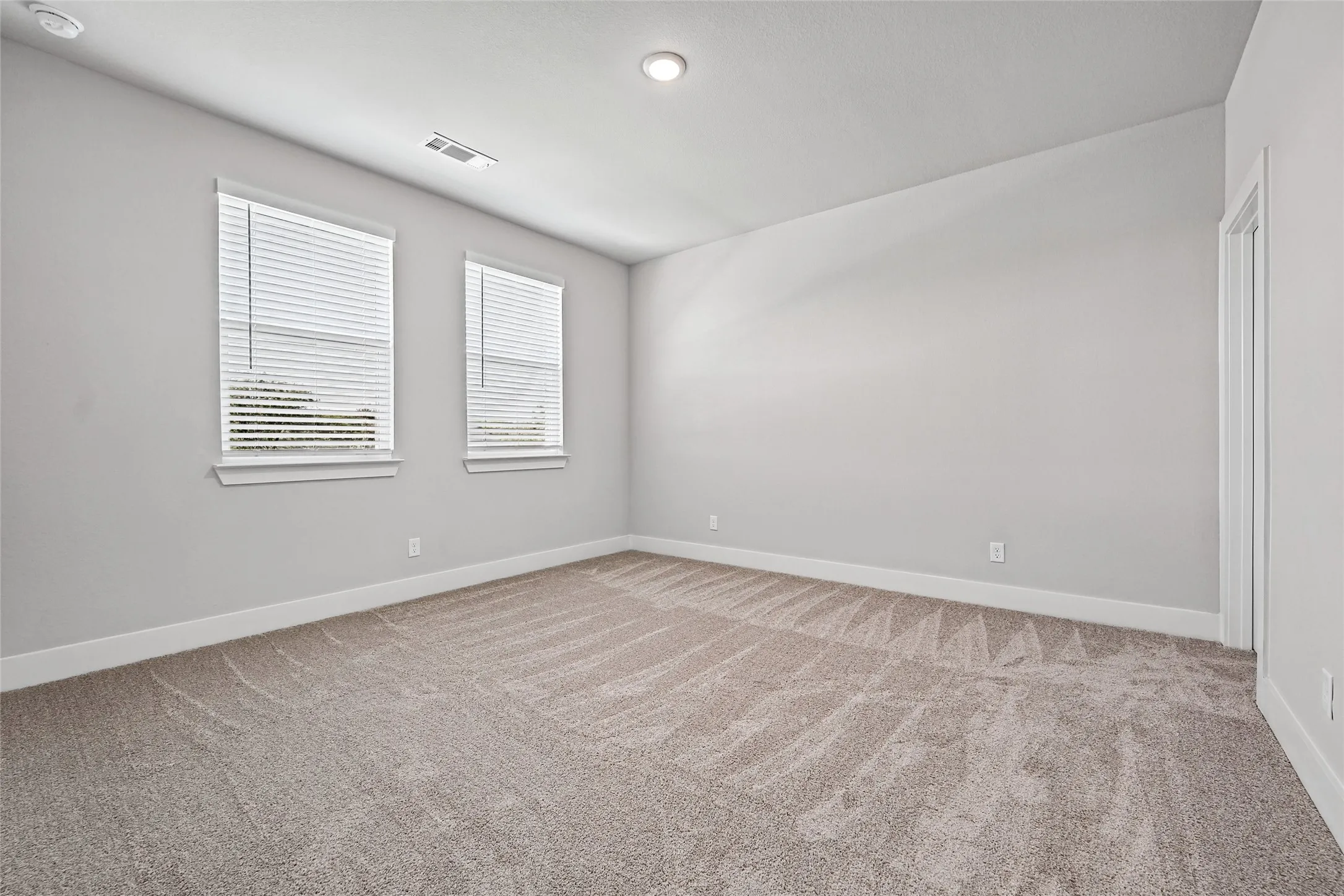 Recessed lighting, light gray wall finish, two windows with blinds, neutral tone carpet flooring, white trim