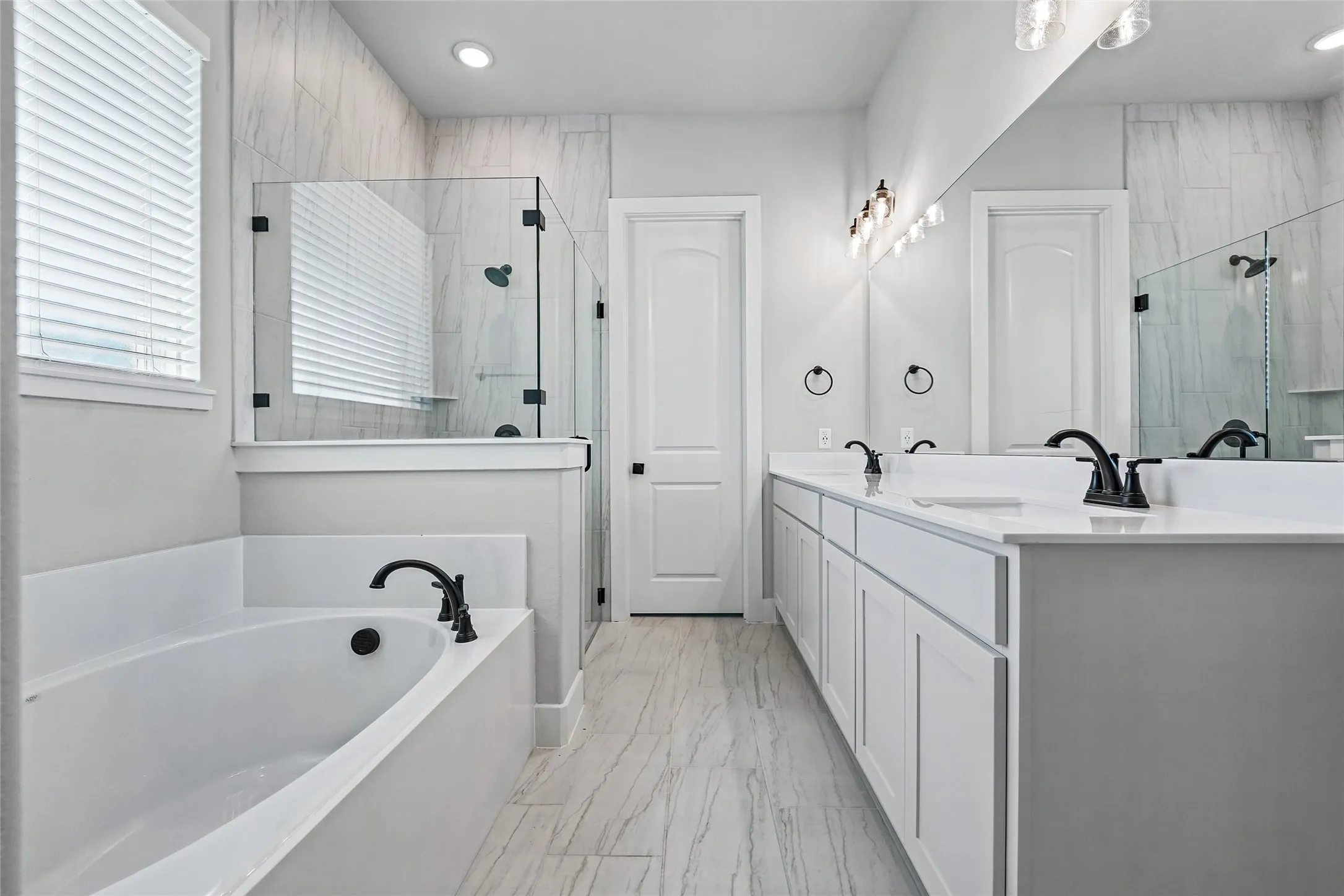 Spacious bathroom with a double vanity, white cabinetry, integrated soaking tub, and a glass-enclosed shower with tiled walls