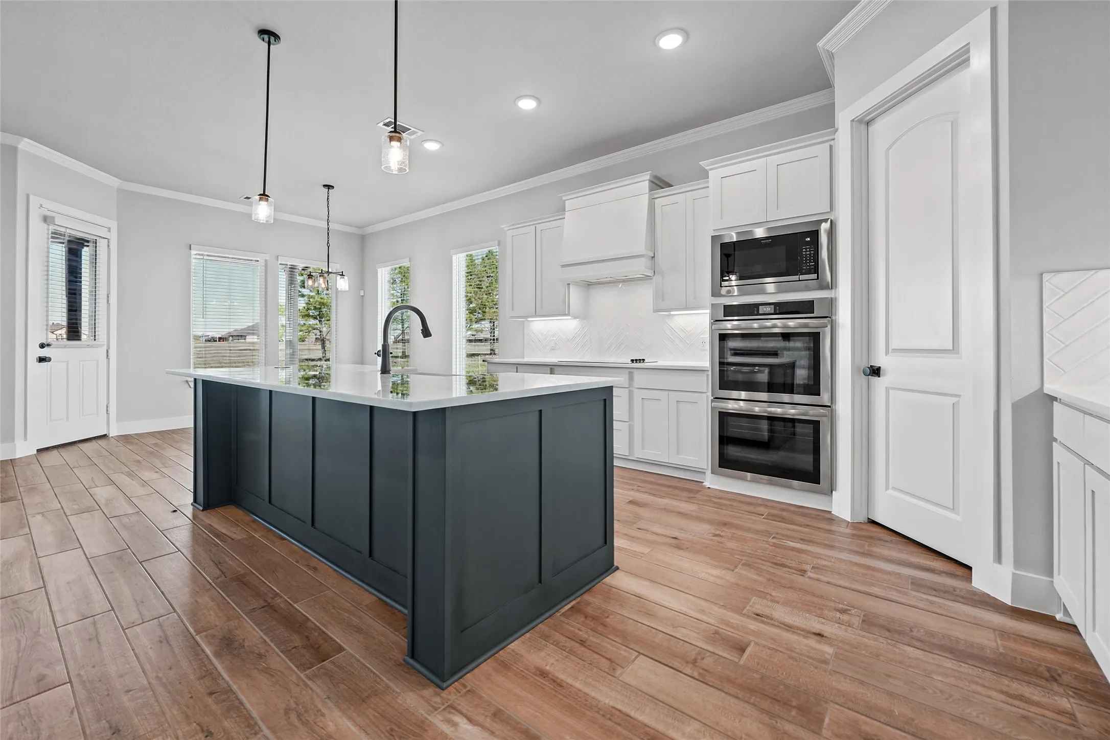Kitchen featuring a dark-toned island with a light-toned countertop, wood-finish flooring, white cabinetry, and stainless steel built-in appliances