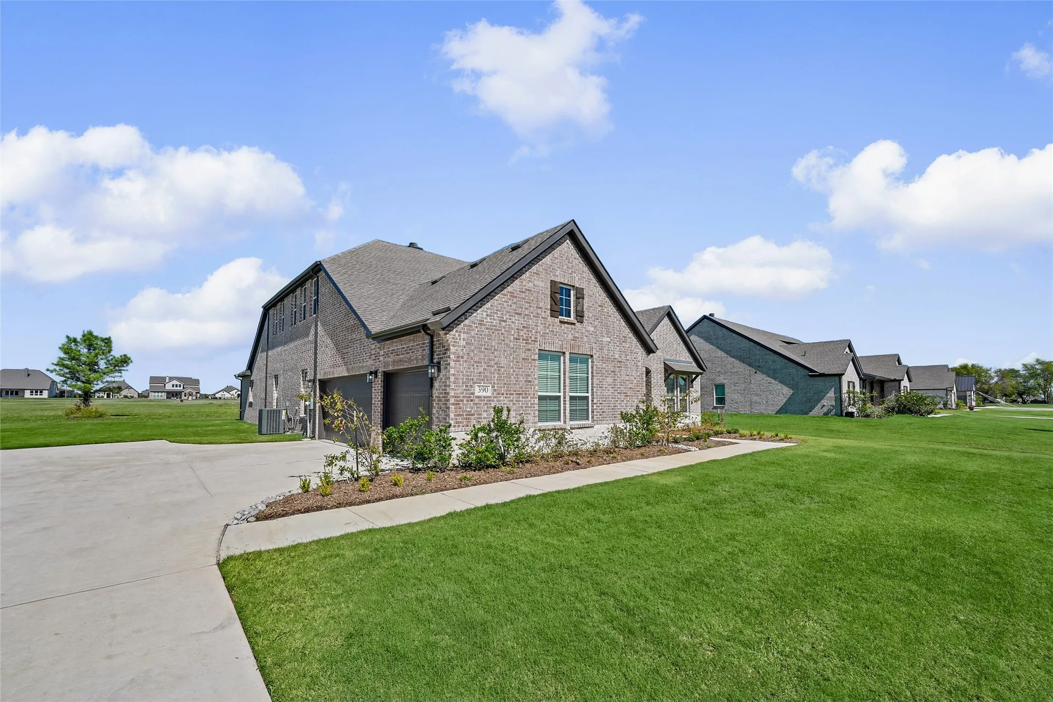 Brick exterior, gabled roofline, concrete driveway, landscaped front beds, and a manicured lawn