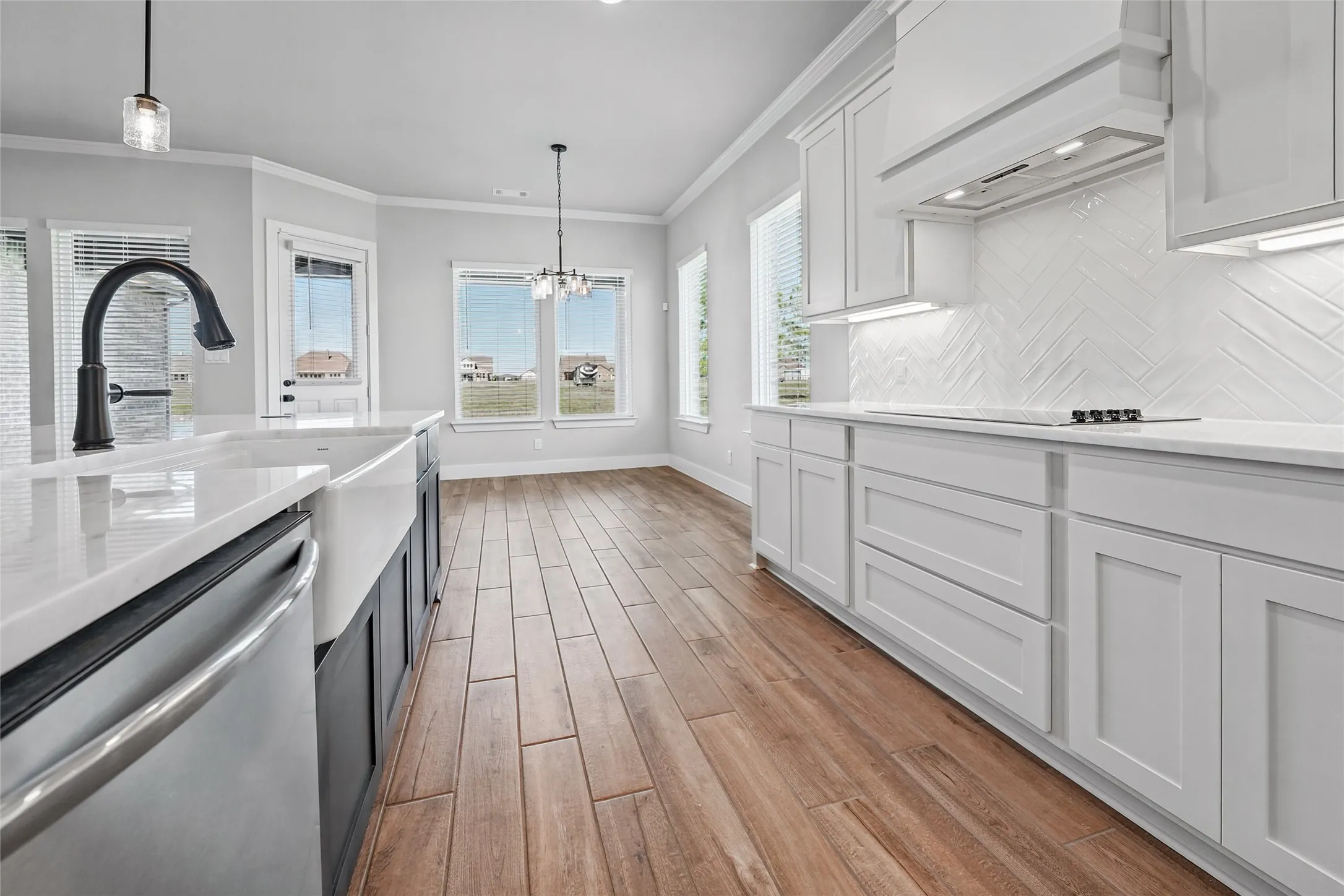Modern kitchen with wood-finish flooring, white cabinetry, integrated range hood, and a farmhouse sink