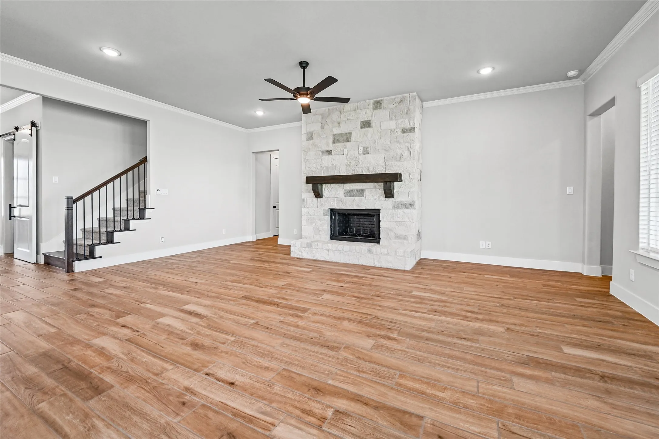 Open-concept living area with wood-finish flooring, stone-clad fireplace, and recessed lighting