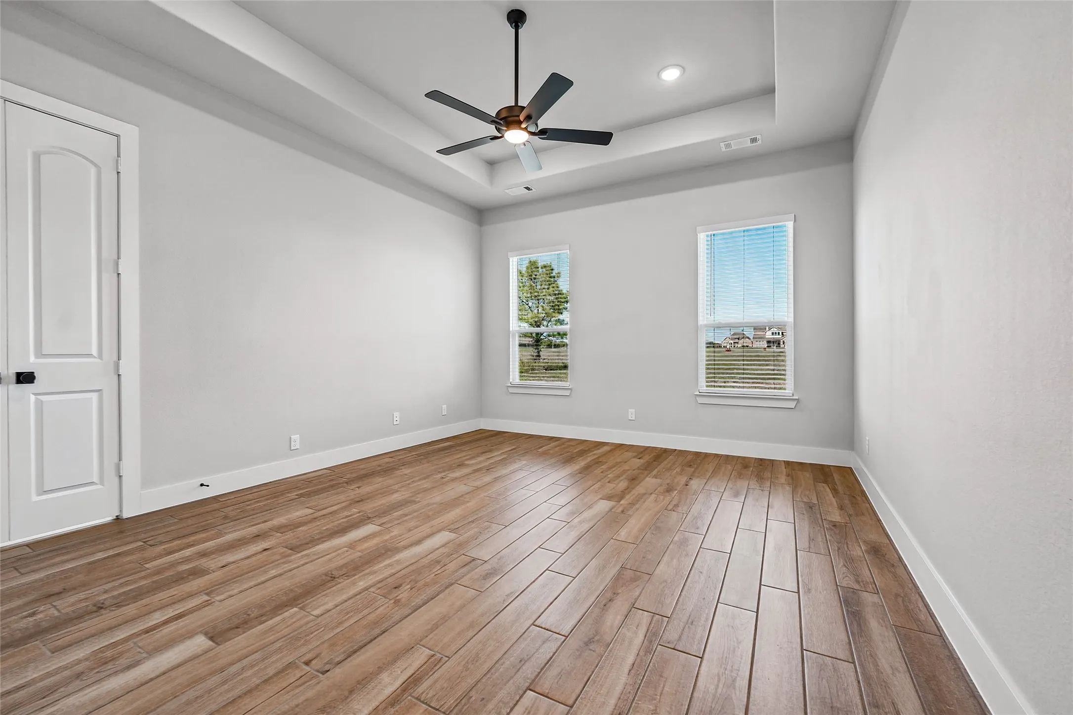 Tray ceiling with recessed lighting, wood-finish flooring, and two windows with horizontal blinds