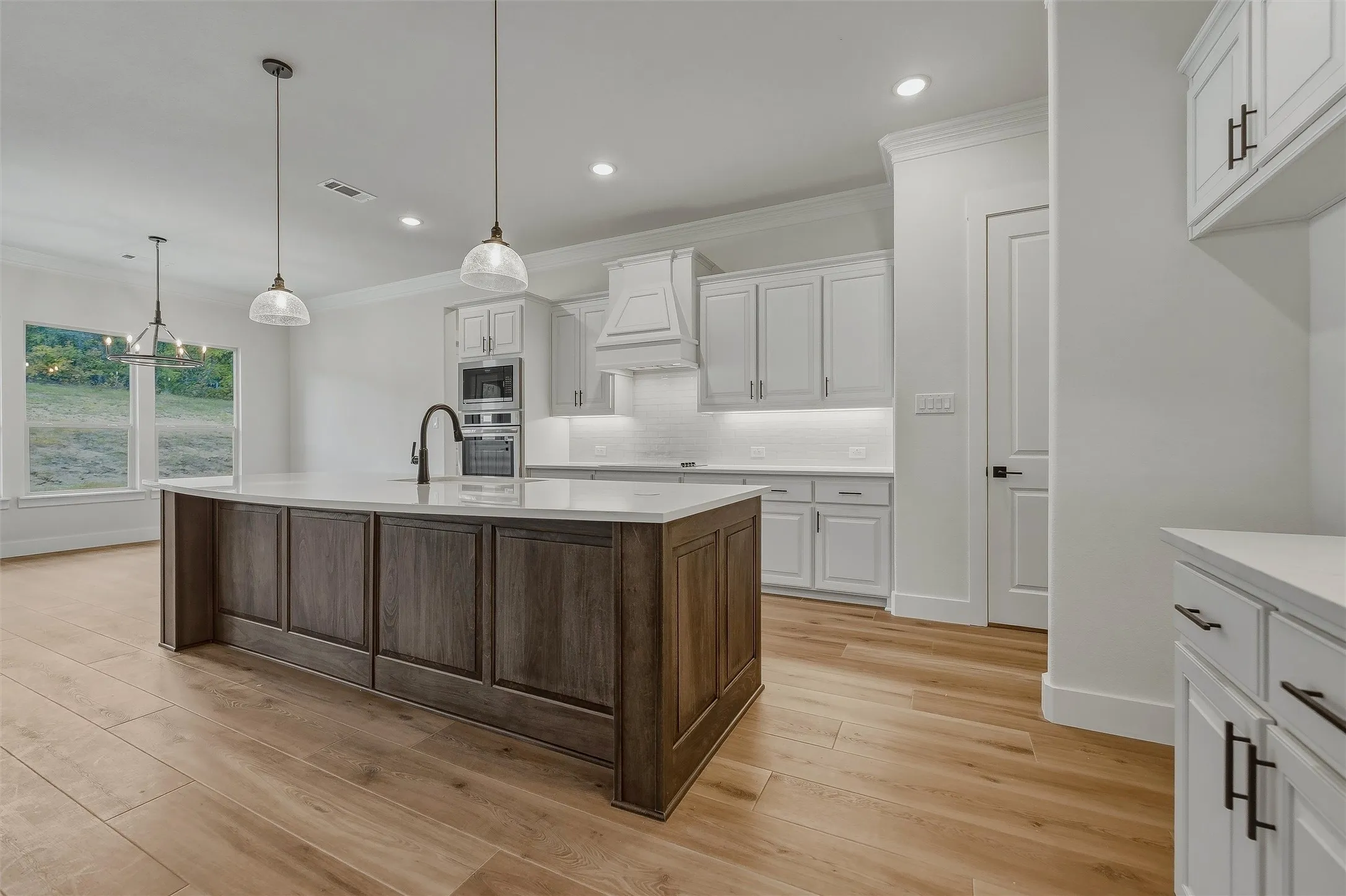 Spacious kitchen featuring a large wood-finish island, light wood-finish flooring, white cabinetry, built-in appliances, and pendant lighting