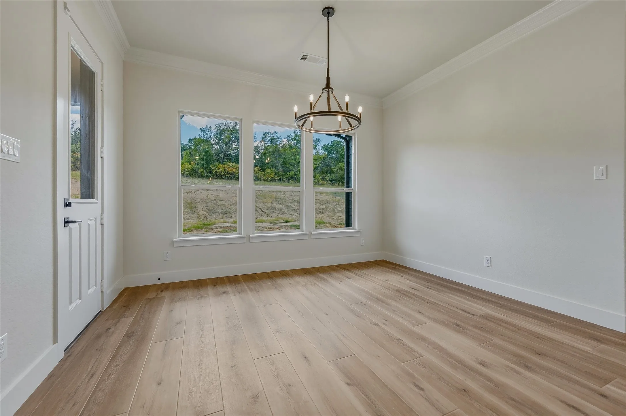 Spacious room featuring wood-finish flooring, multiple windows, a modern chandelier, and a paneled door with a clear glass insert