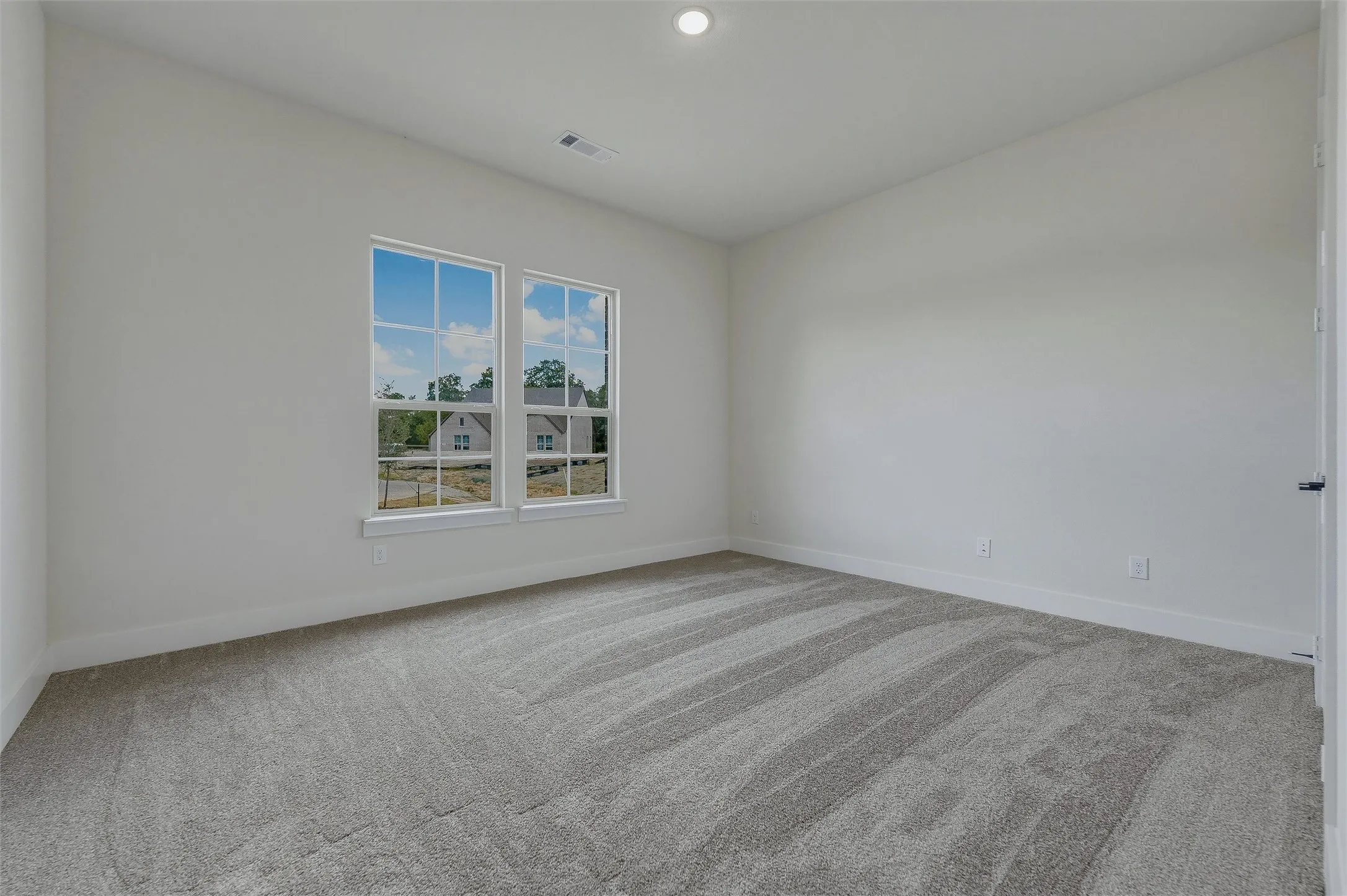 Dual windows, recessed lighting, and light gray patterned carpet