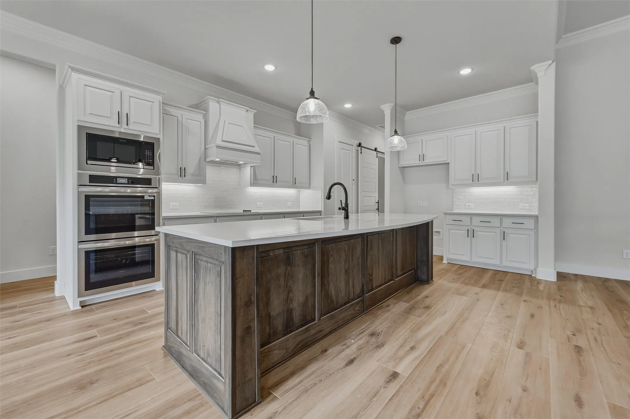 Kitchen featuring a two-tone island with a light-toned countertop, wood-finish flooring, white cabinetry, stainless steel double ovens, and a built-in microwave