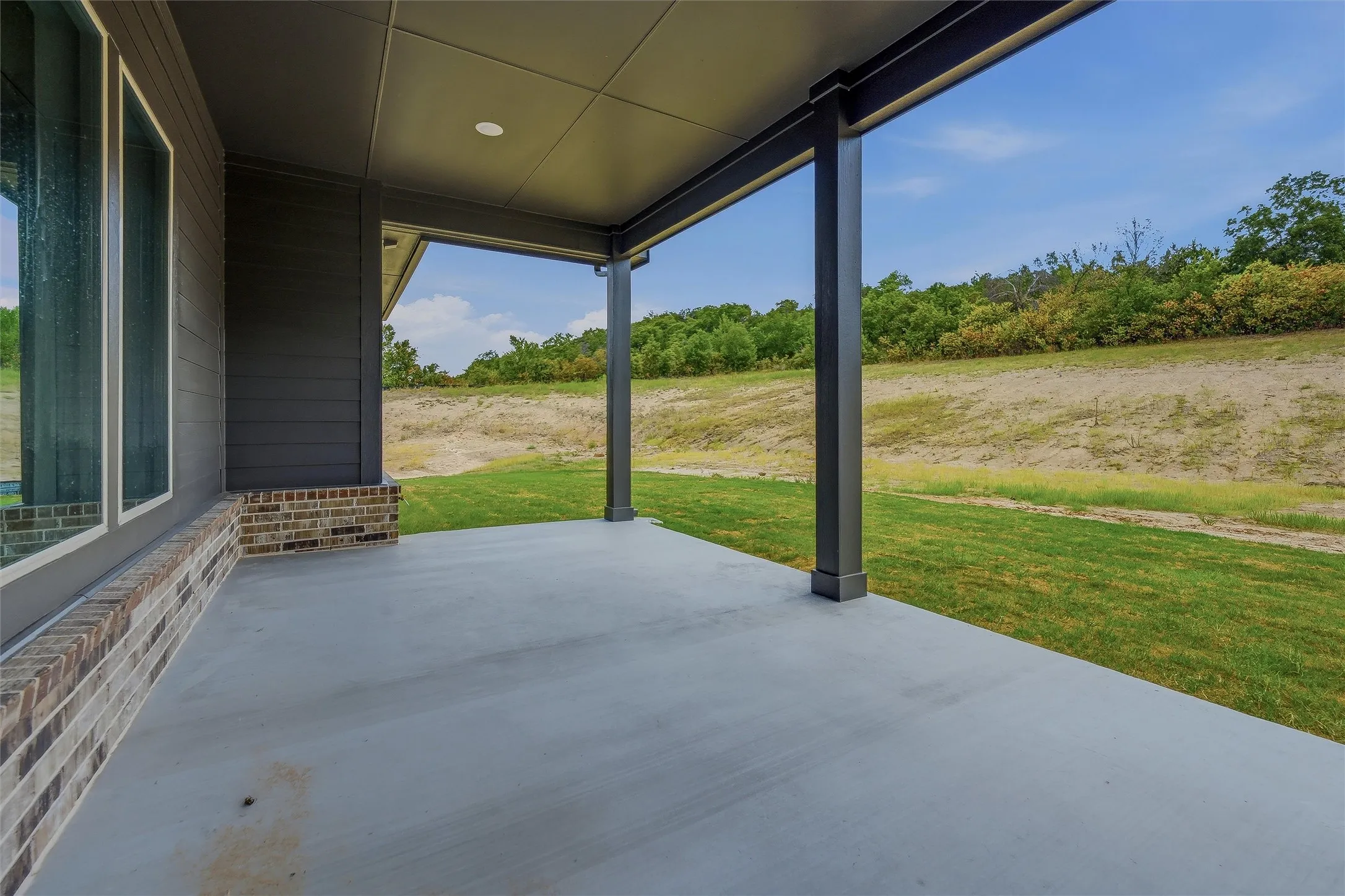 Expansive covered patio with concrete flooring, recessed lighting, and structural columns
