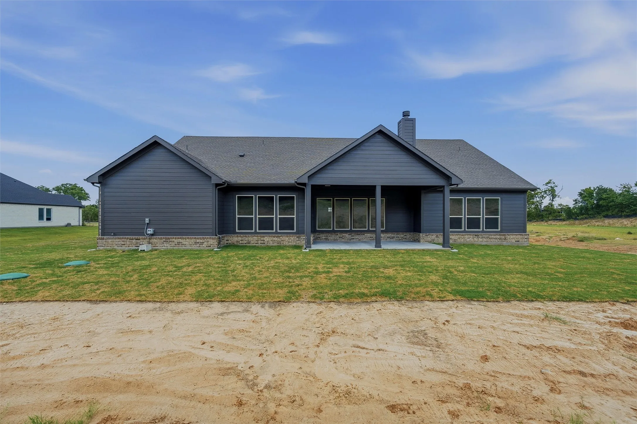Dark gray siding with brick-finish foundation, multiple window sets, a covered patio, and a shingle roof