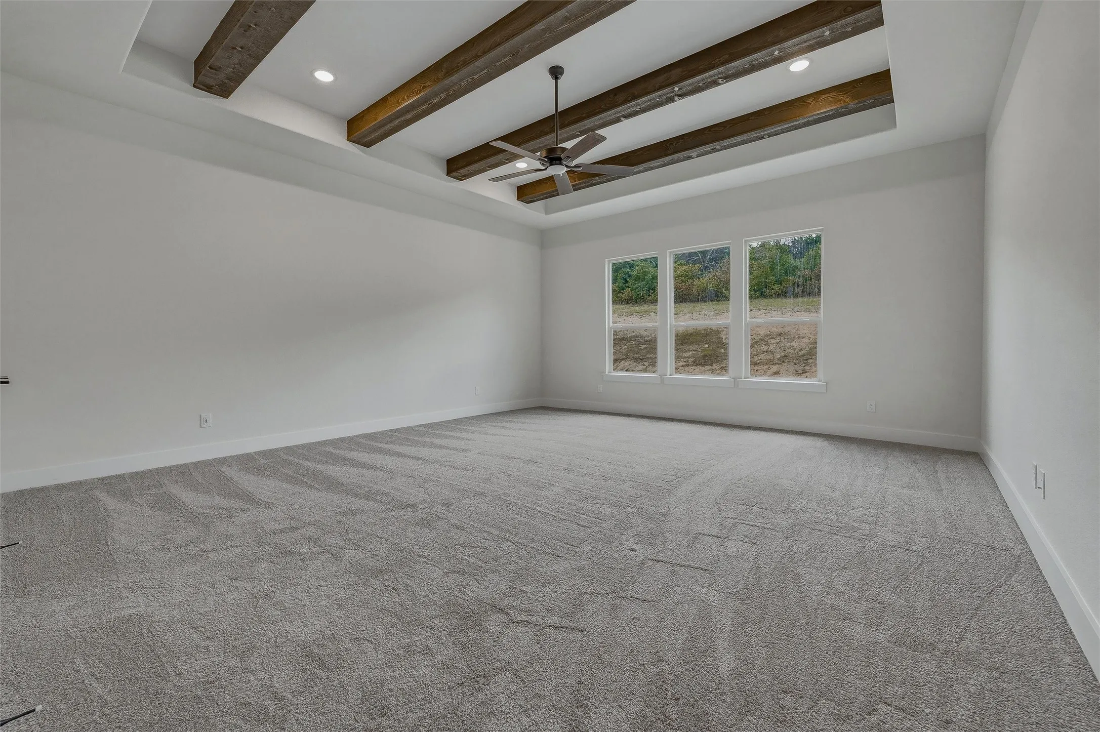 Tray ceiling with wood-finish beams, recessed lighting, ceiling fan, triple windows, and neutral carpeting