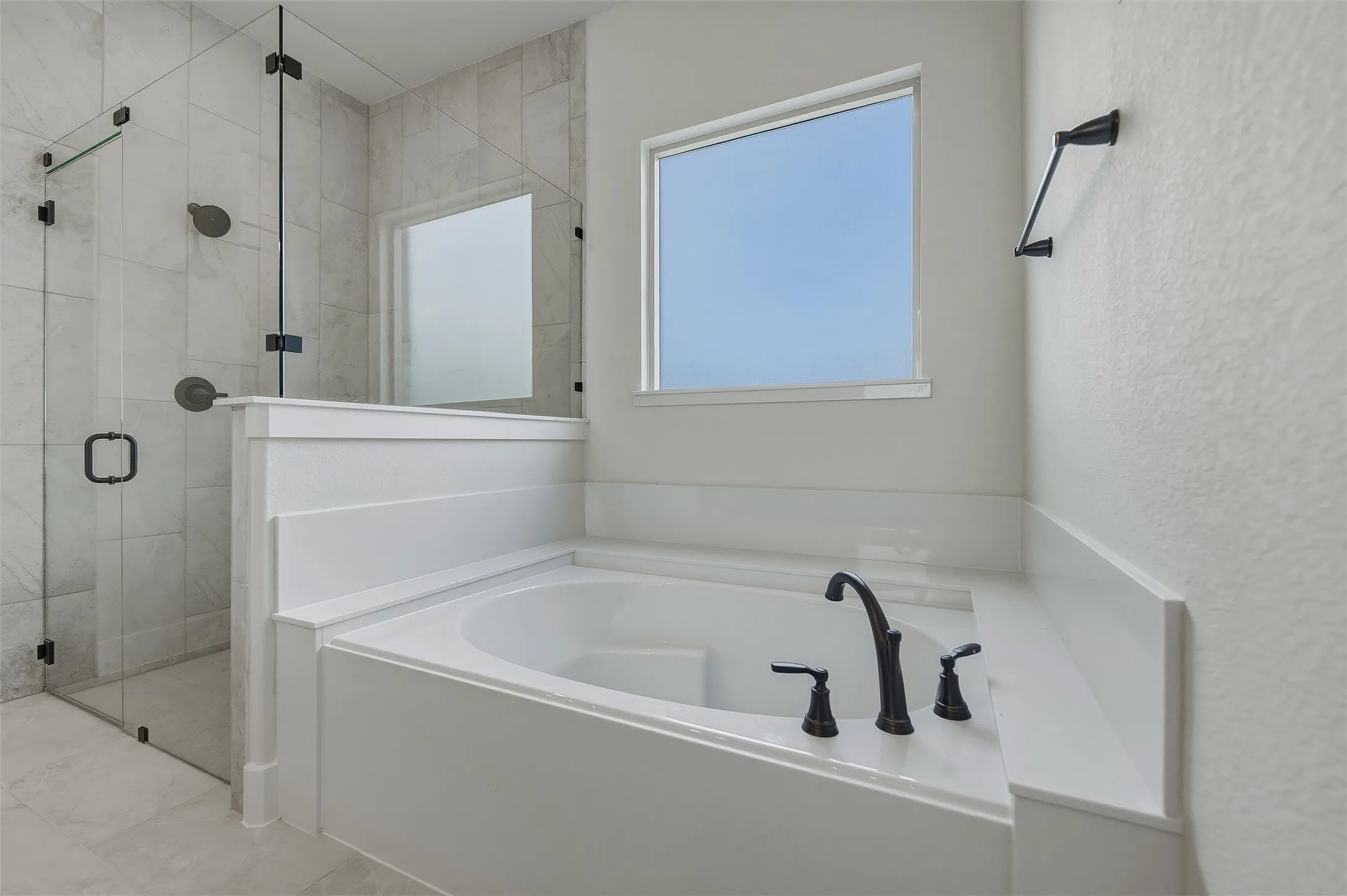 Soaking tub with matte black fixtures, tile-surround shower with glass enclosure, and white wall paneling