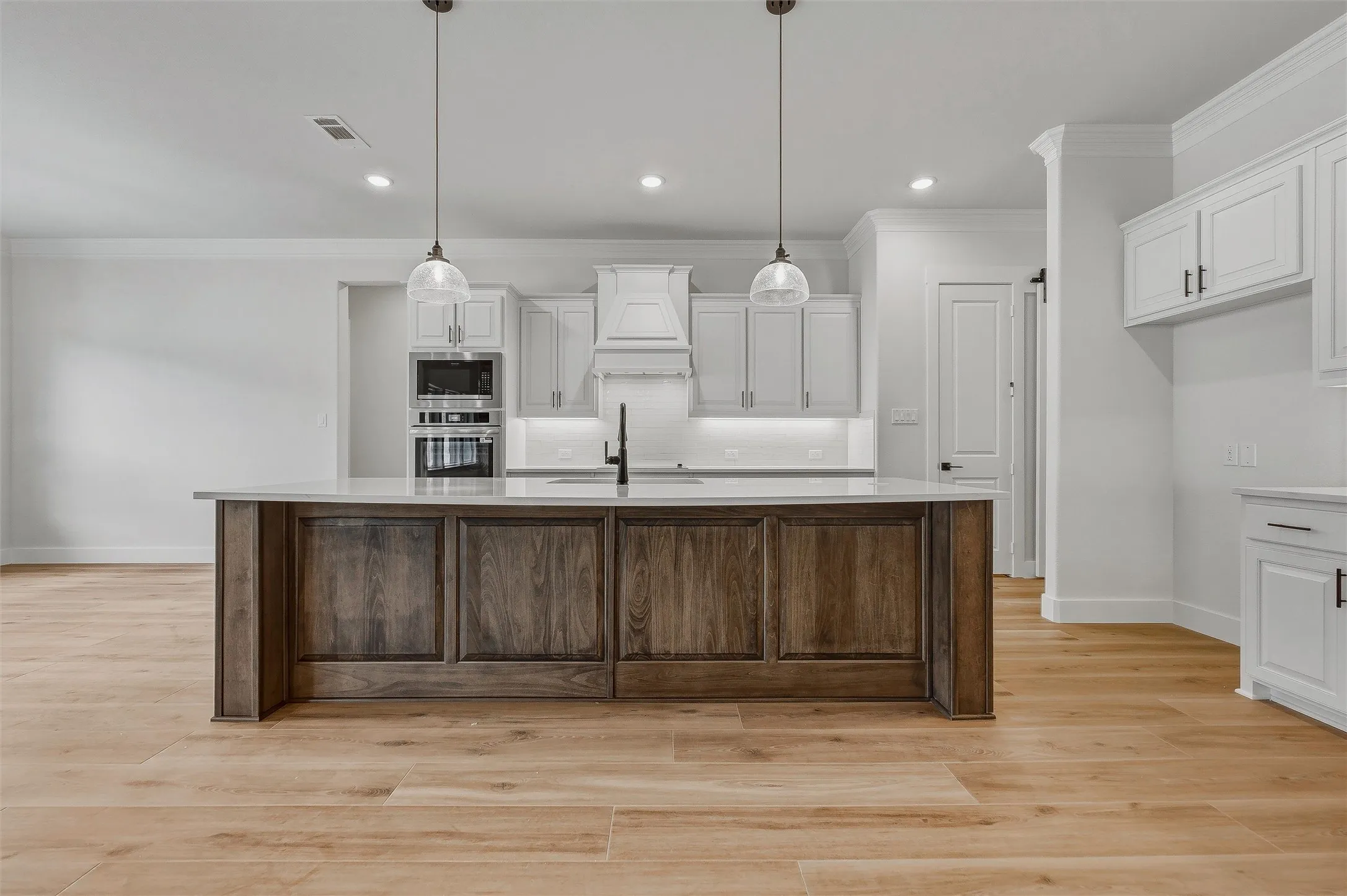 Kitchen featuring a wood-finish island with a light-toned countertop, white cabinetry with dark hardware, recessed lighting, and matching pendant lights