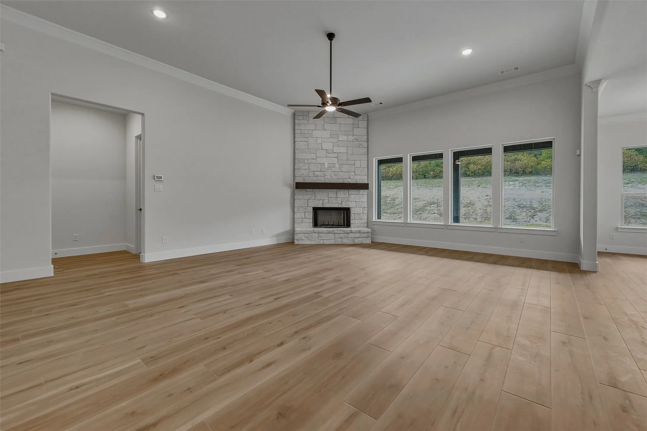 Vaulted ceiling with recessed lighting, wood-finish flooring, stone-clad fireplace with wood mantel, multiple large windows, and a ceiling fan