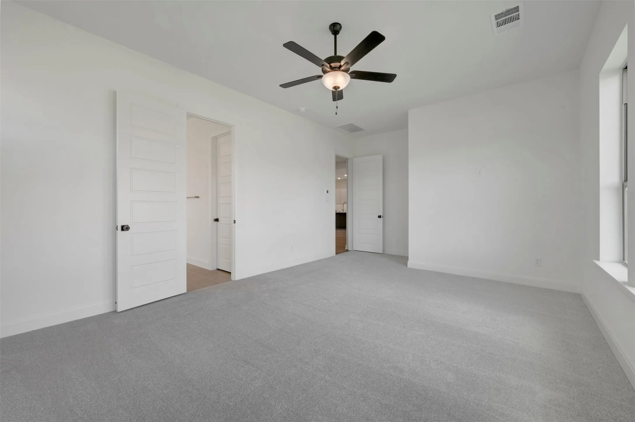 Spacious room featuring gray carpeting, white walls, a ceiling fan with integrated lighting, and a window with a deep sill