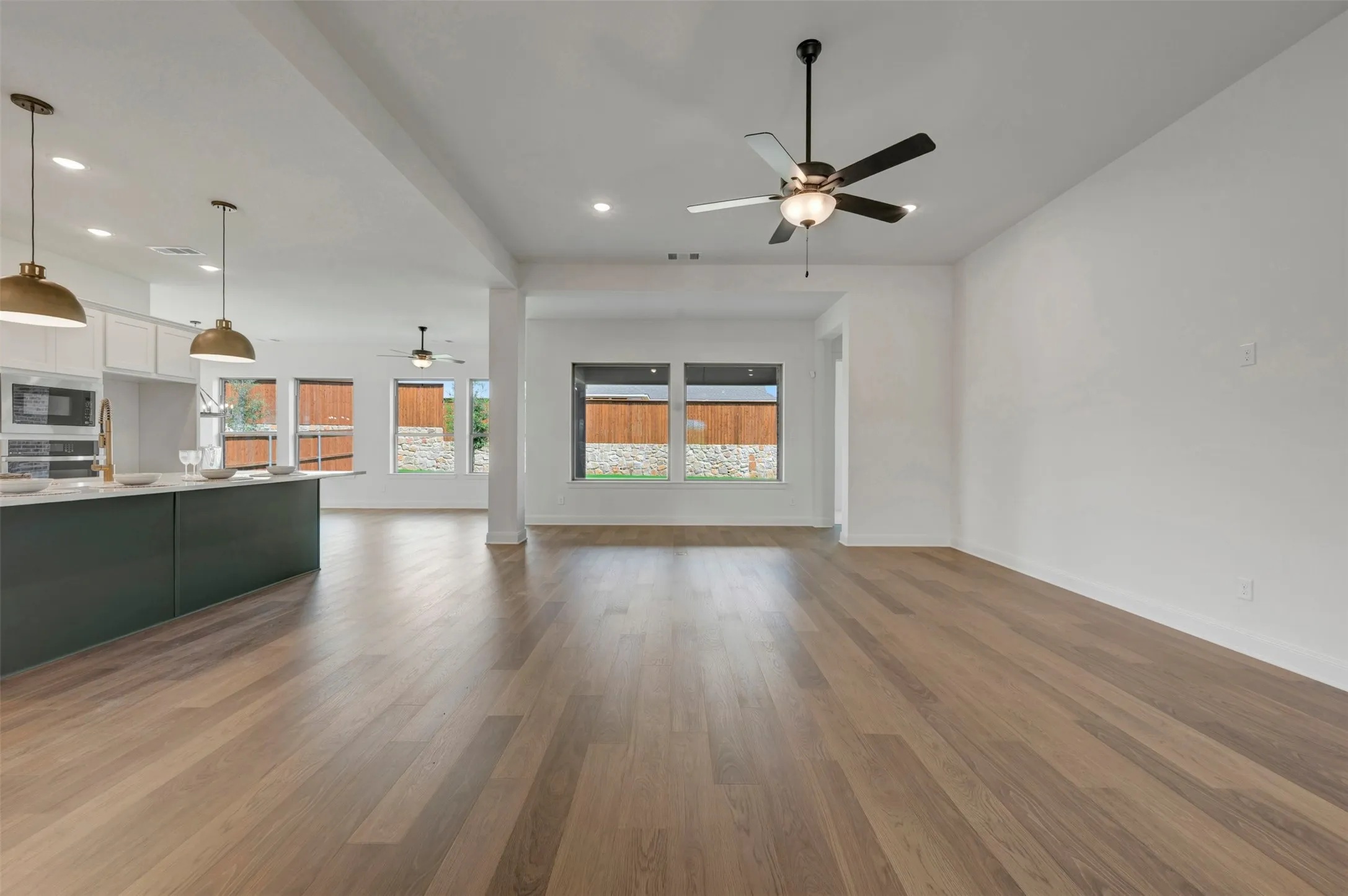 Wood-finish flooring throughout, recessed lighting, ceiling fan, kitchen island with dark cabinetry, and white overhead cabinetry
