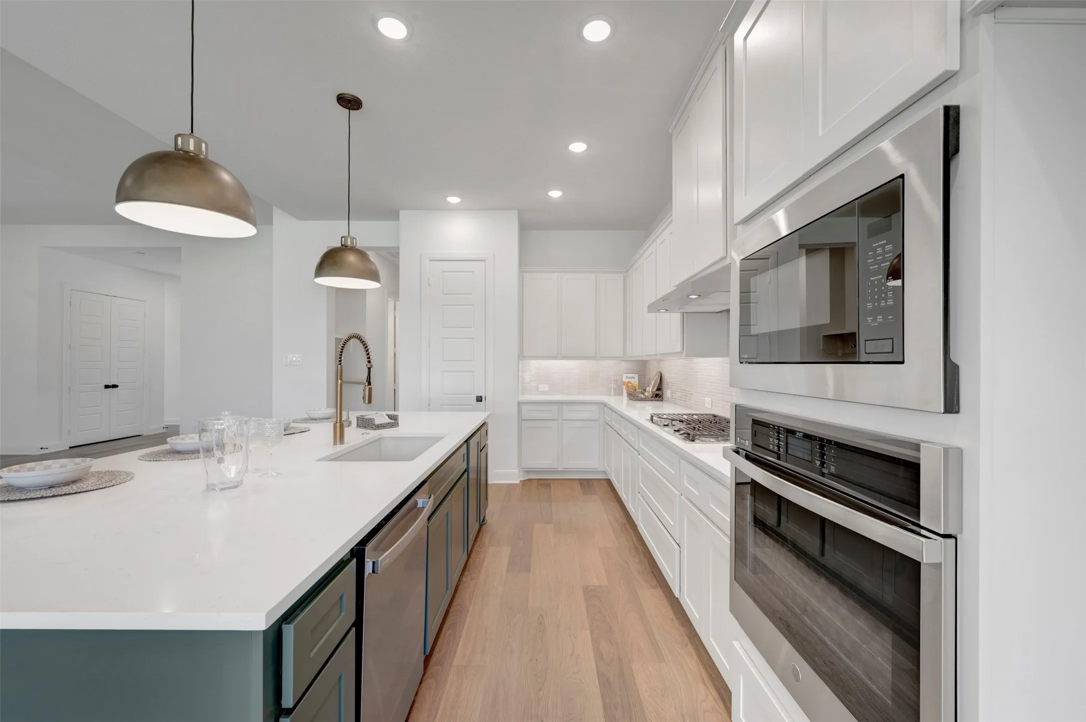 Kitchen featuring an elongated island with a built-in sink, stainless steel appliances, pendant lighting, recessed lighting, and wood-finish flooring
