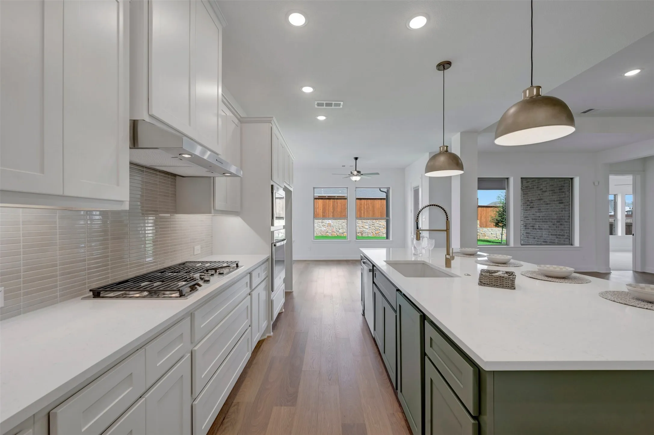 Contemporary kitchen featuring white cabinetry, a gas range with a stainless steel hood, a large island with a built-in sink, and pendant lighting