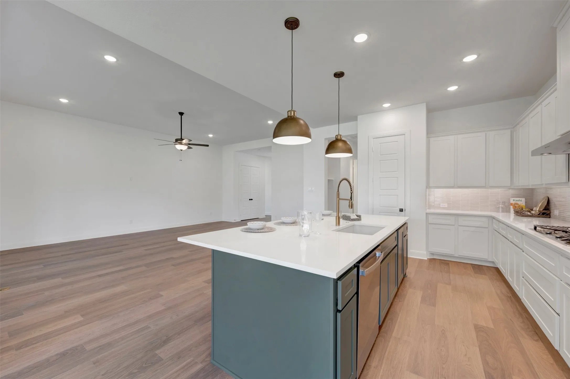 Kitchen island with white countertop, brass pendant lighting, wood-finish flooring, white cabinetry, and stainless steel appliances