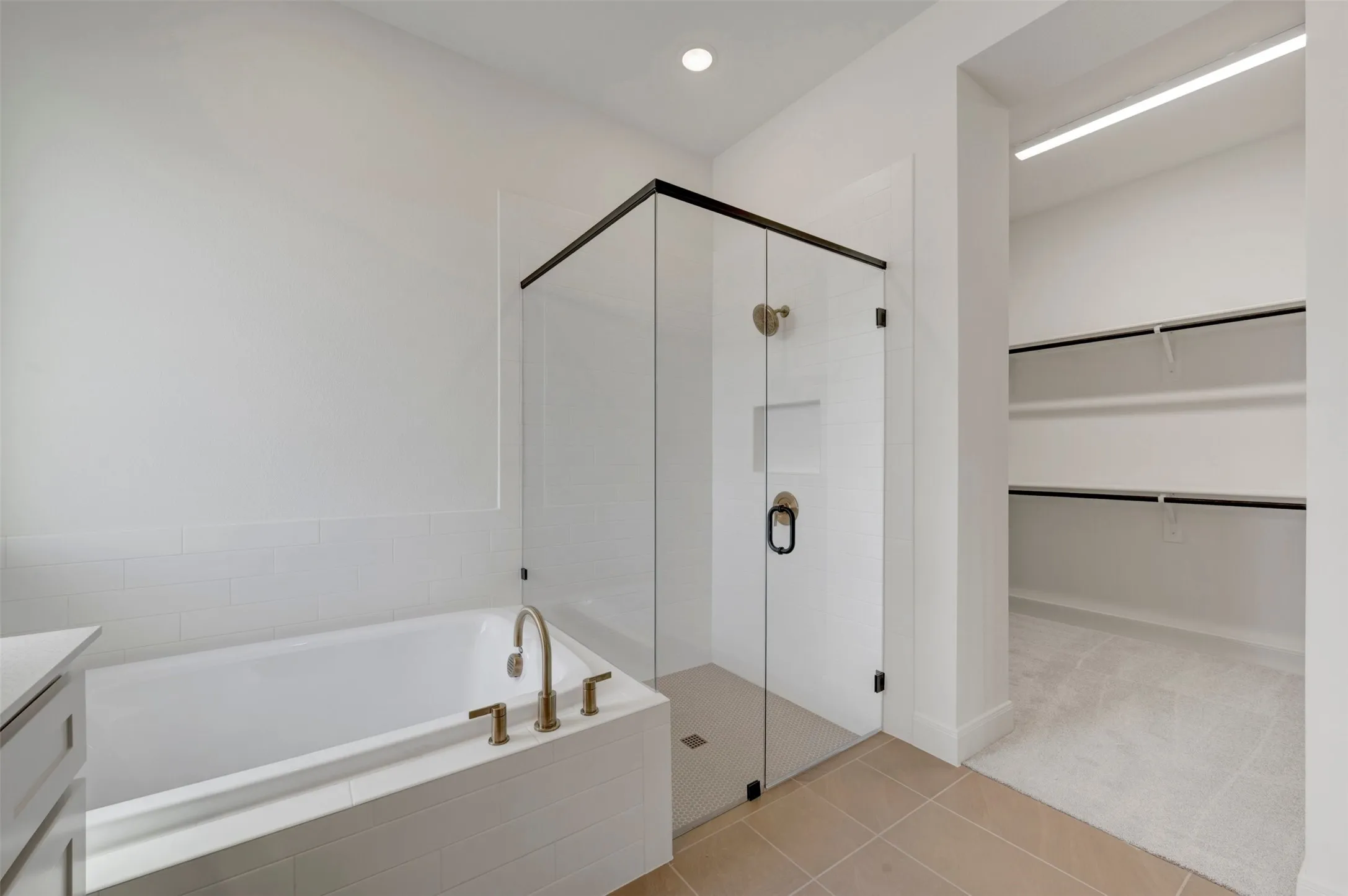Built-in soaking tub with gold-tone fixtures, glass-enclosed shower with a matte black frame, and a spacious walk-in closet with integrated shelving