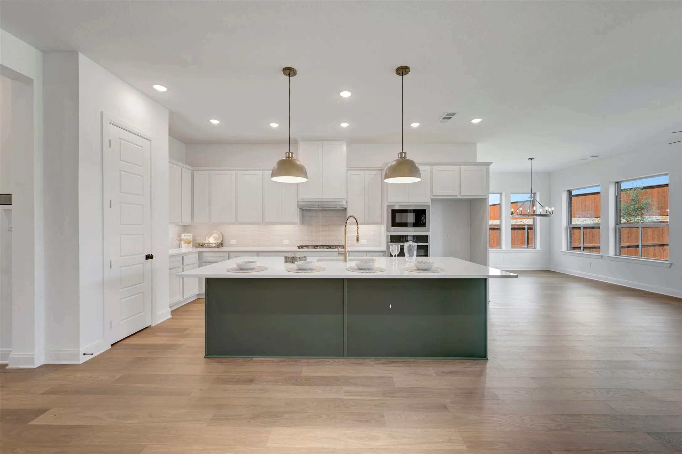 Open-concept kitchen with a large central island, pendant lighting, built-in appliances, and wood-finish flooring throughout