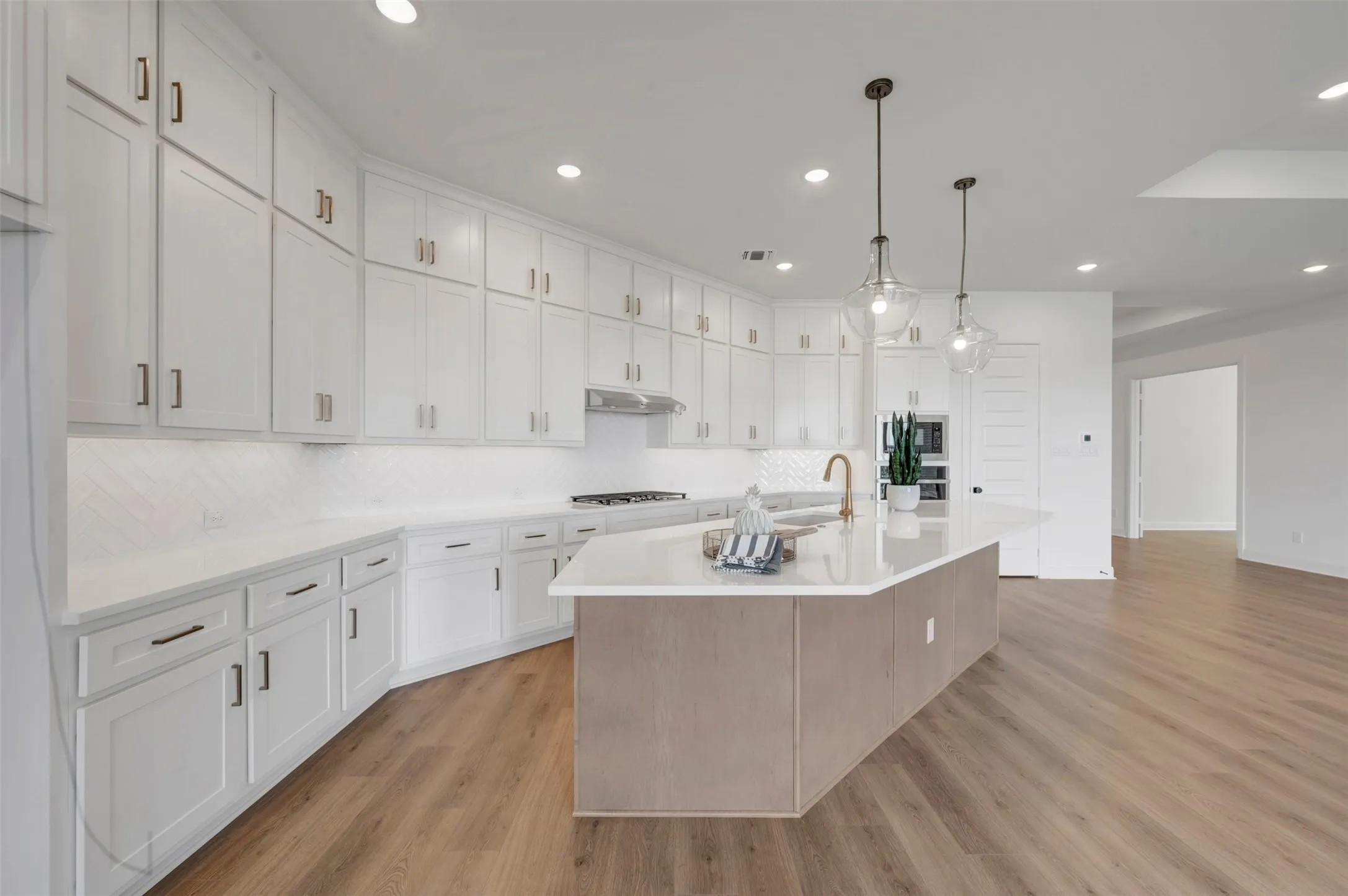 White cabinetry with brass hardware, undermount sink with a brass faucet, white countertop, wood-finish flooring, and pendant lighting