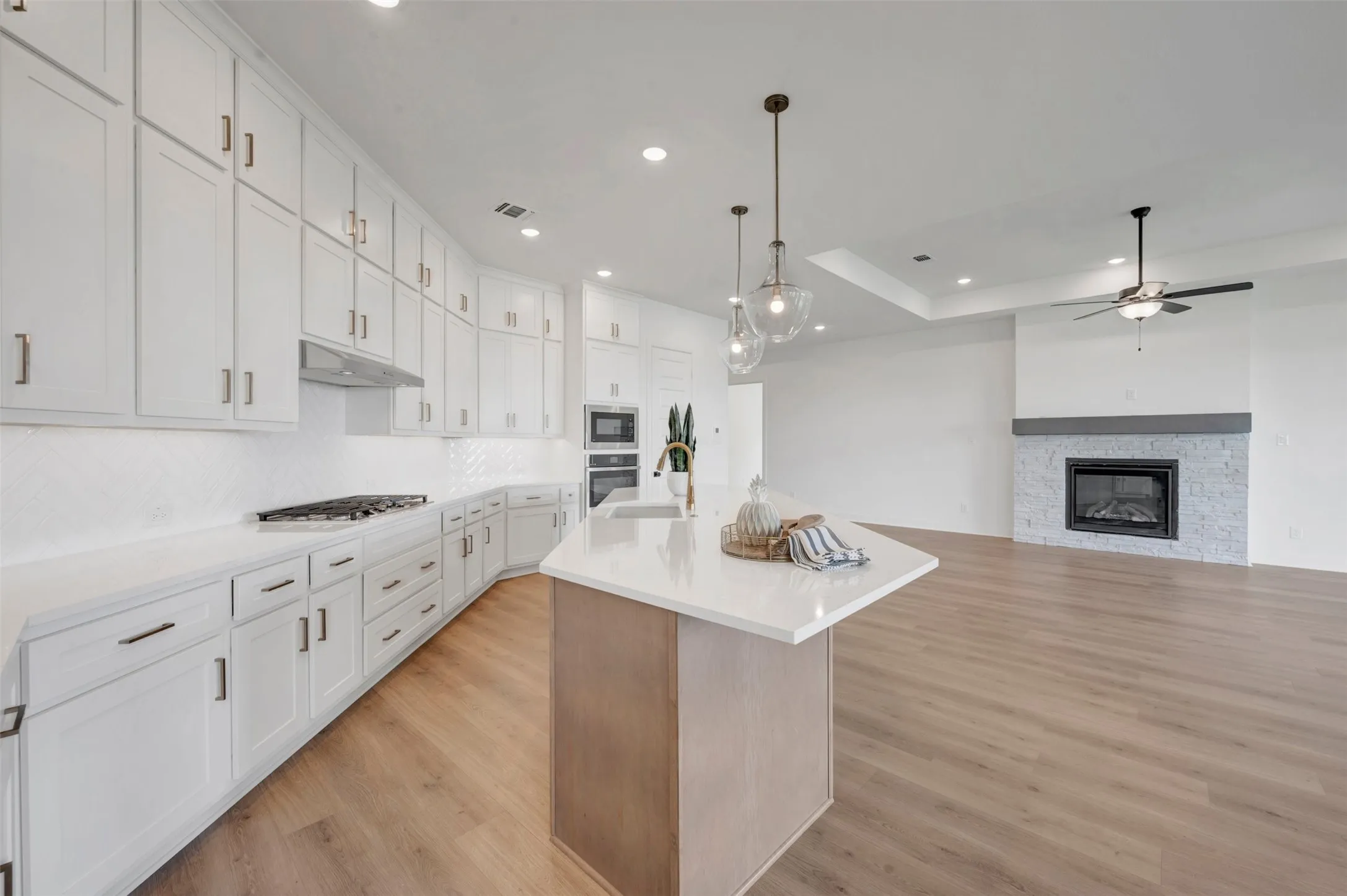 White cabinetry with modern hardware, recessed lighting, wood-finish flooring, kitchen island with a white countertop, and a fireplace with a stone surround