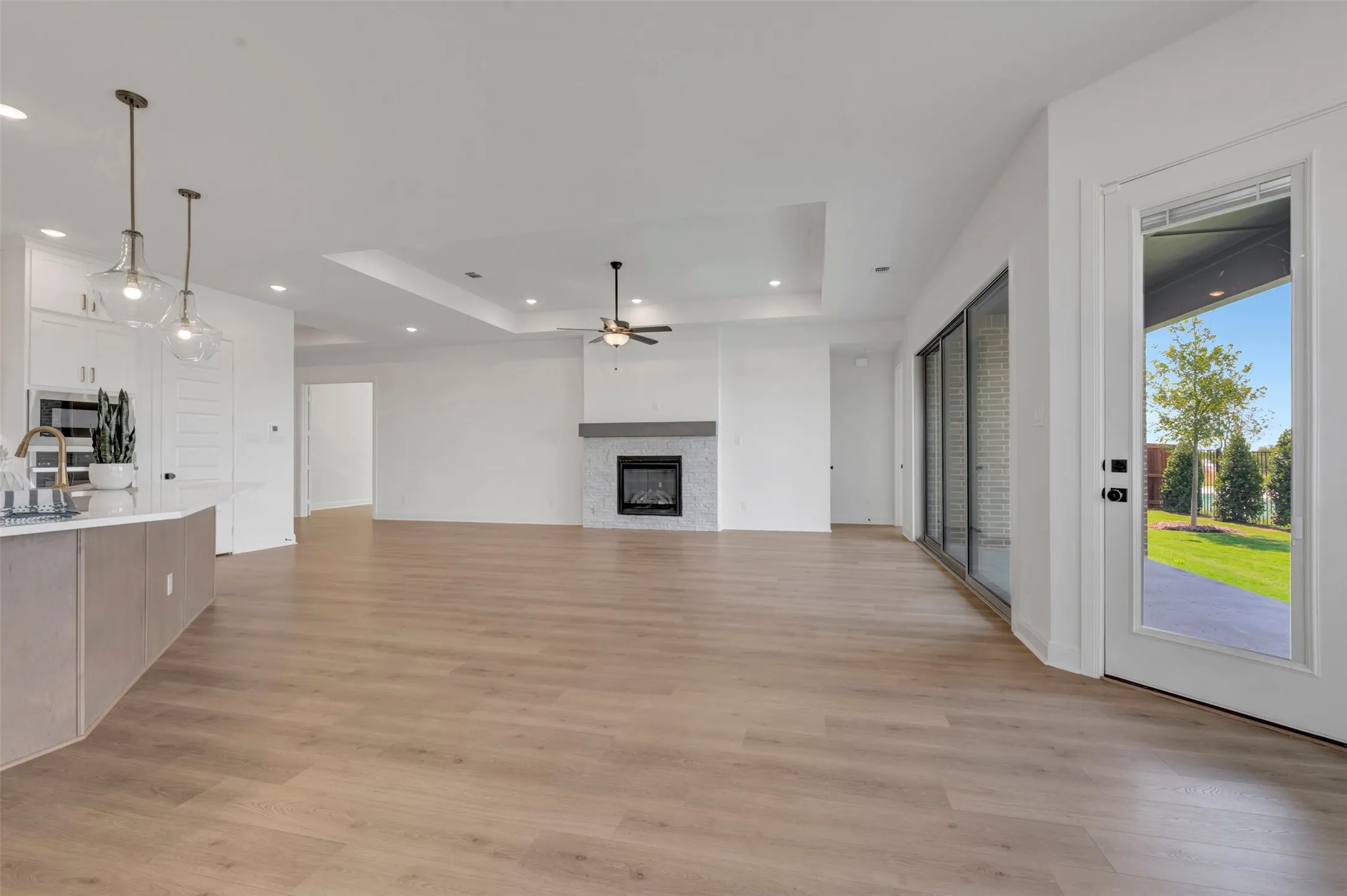 Open-concept living area with wood-finish flooring, a tiled fireplace with a mantel, and a tray ceiling