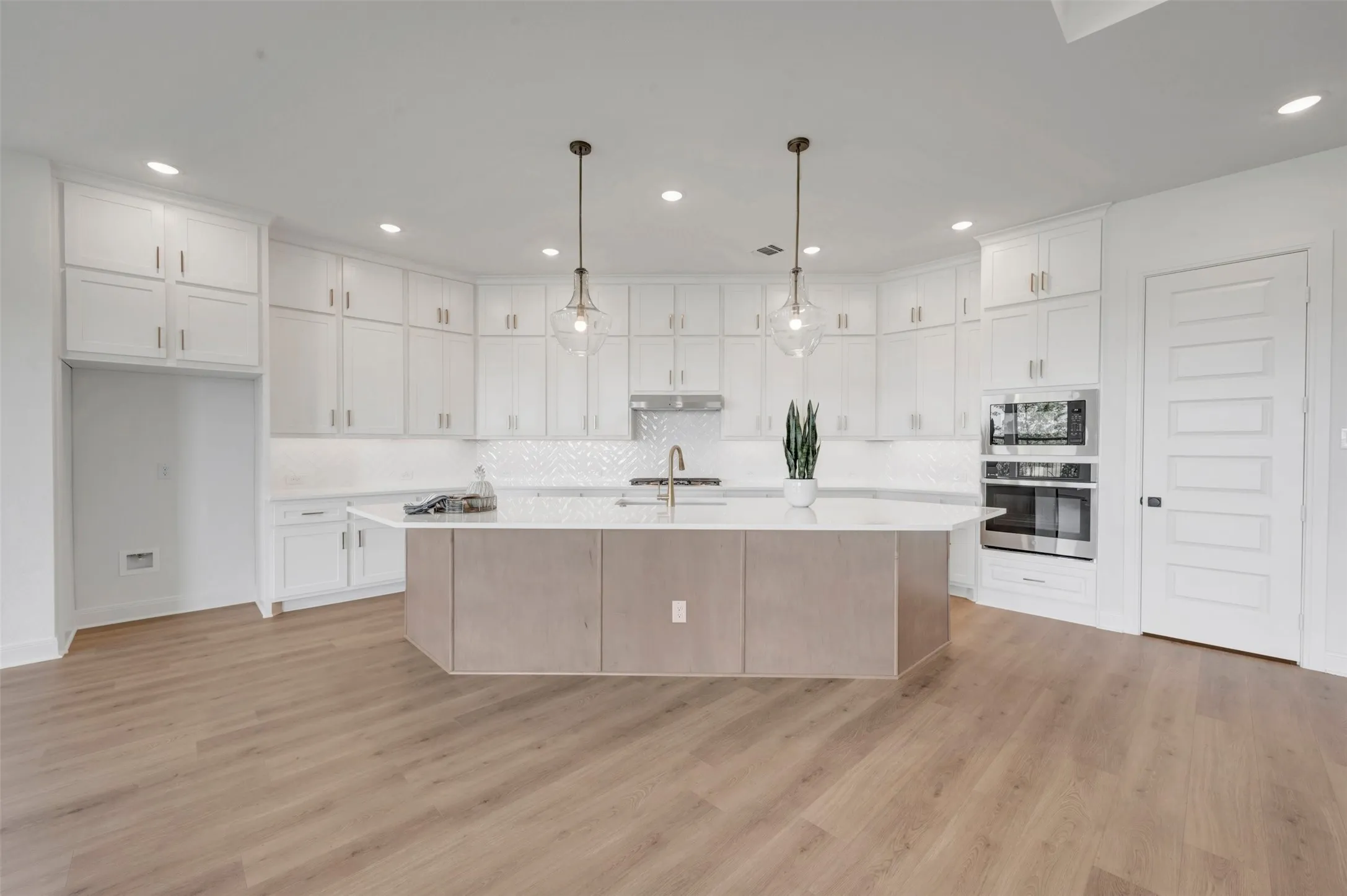 Spacious kitchen featuring an expansive center island, white cabinetry, built-in stainless steel appliances, herringbone tile backsplash, and light wood-finish flooring