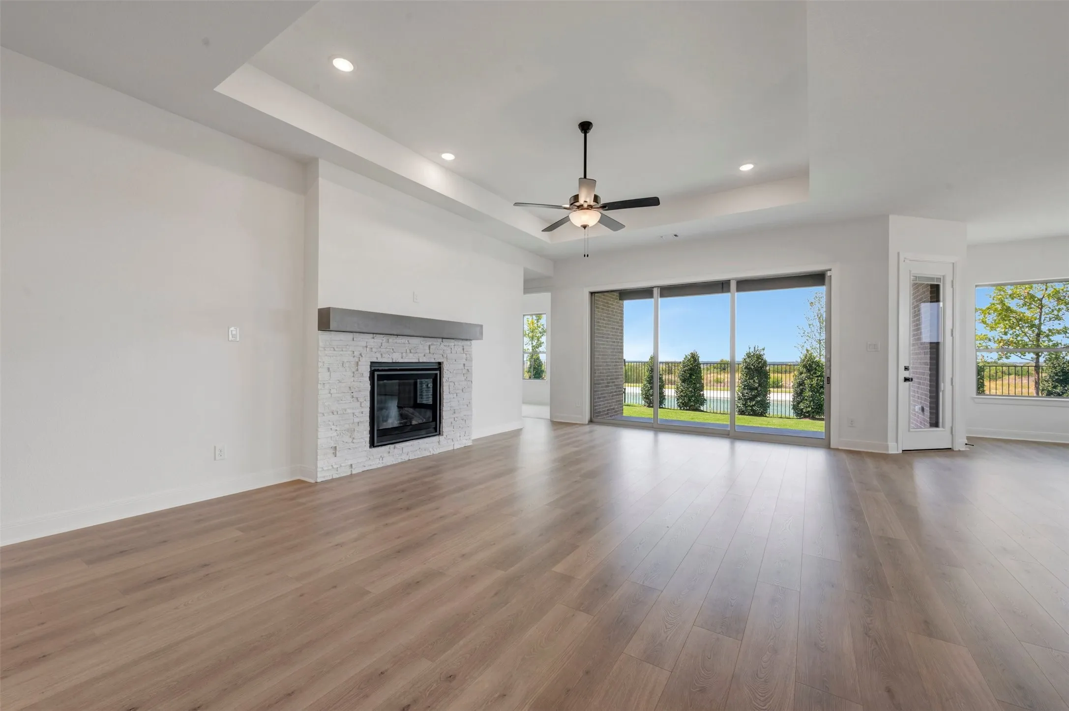 Spacious open-concept living area showcasing refinished wood flooring, a gas fireplace with tile surround, recessed ceiling lighting, and a ceiling fan