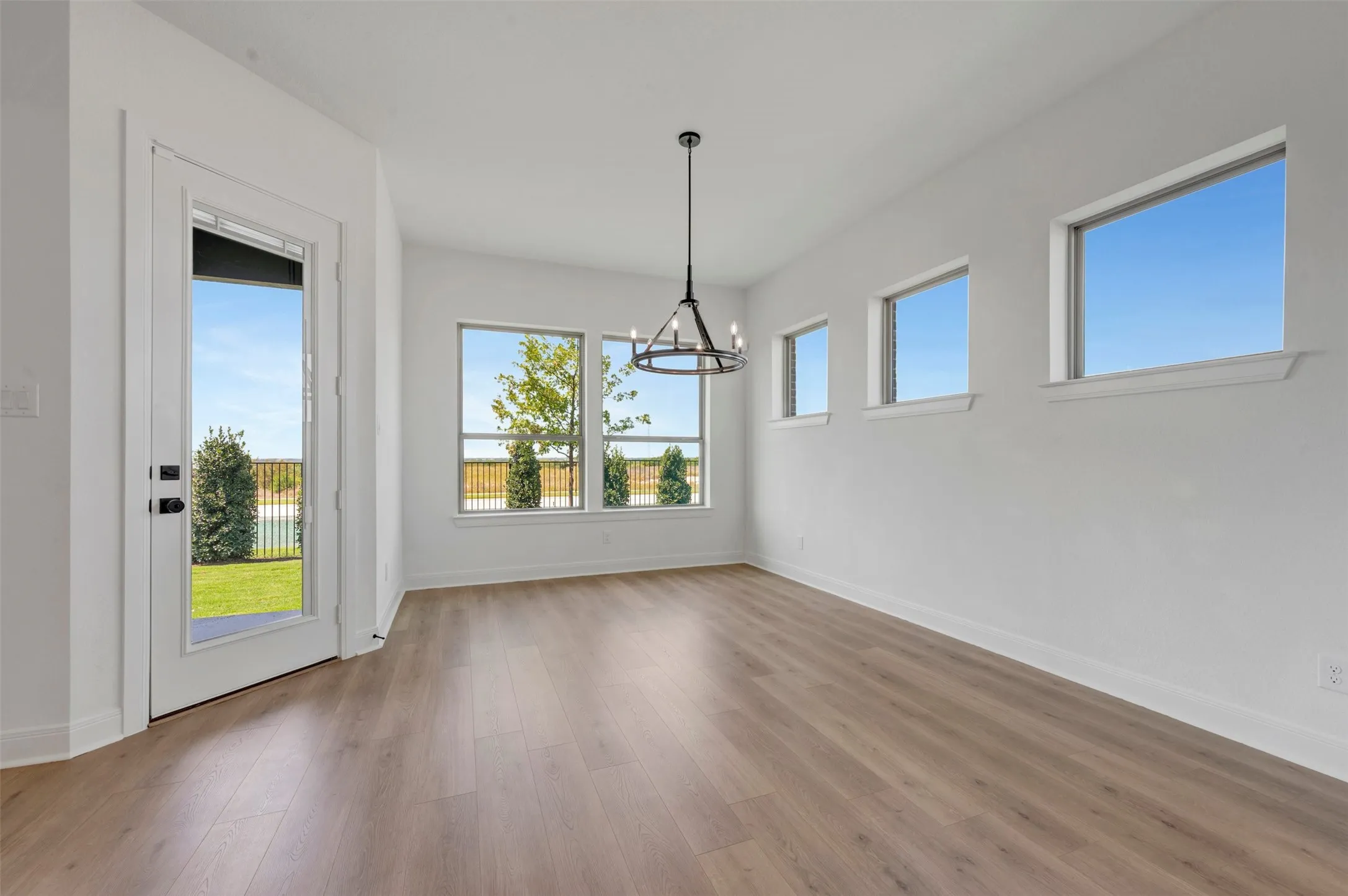Bright, light-filled room featuring engineered wood-finish flooring, abundant natural light from multiple windows and glass door access to outdoor space, and a modern pendant light fixture suspended from the ceiling