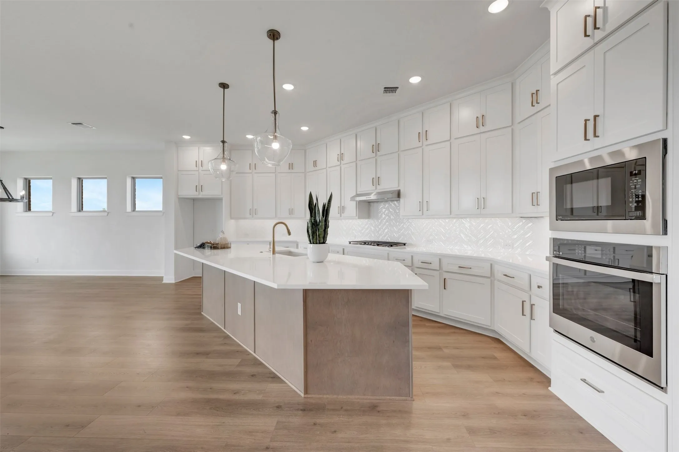 Open-concept kitchen with a substantial island, built-in stainless steel appliances, white cabinetry, and wood-finish flooring