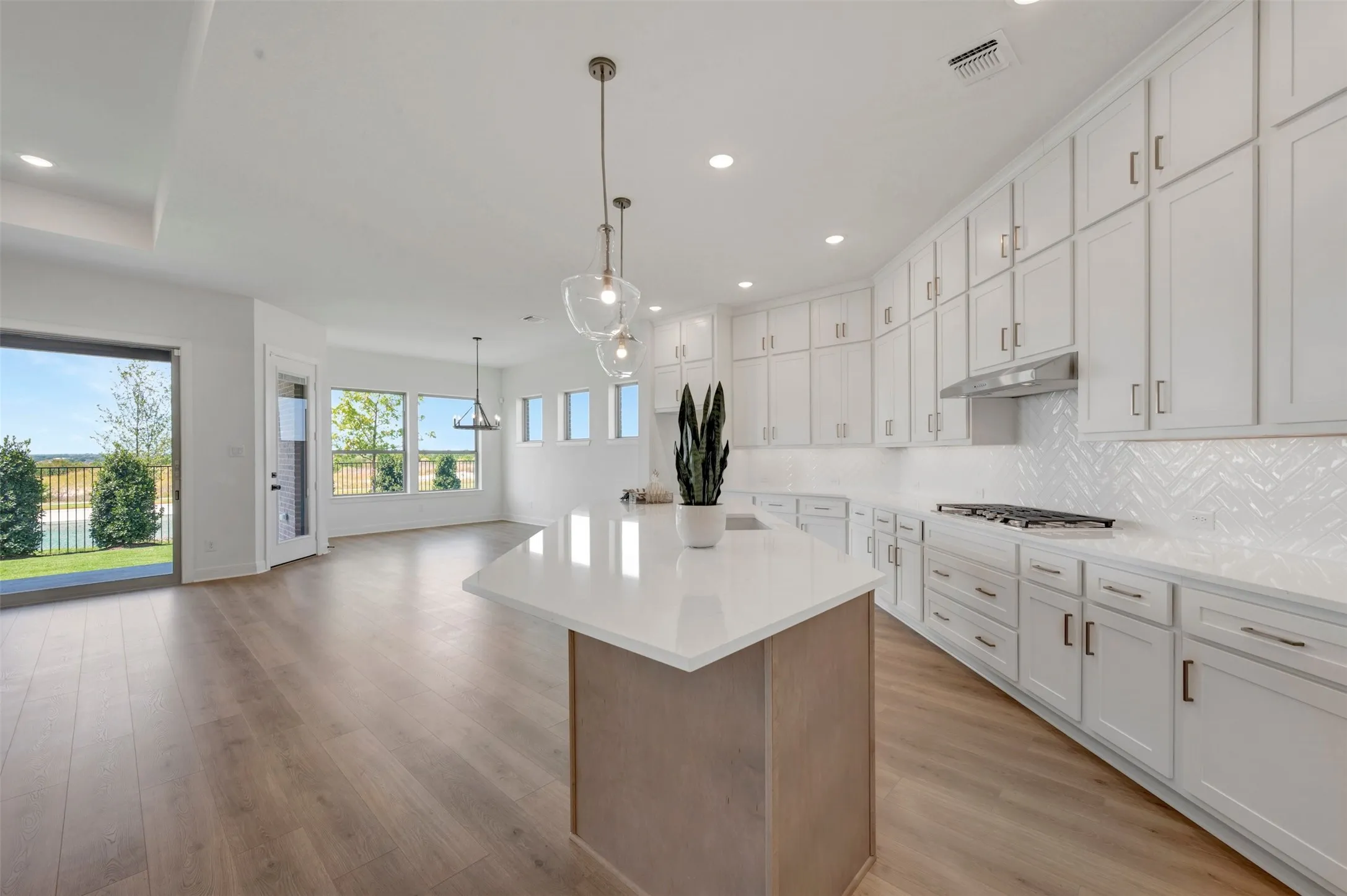 Open-concept kitchen featuring an expansive island with a solid surface countertop, abundant white cabinetry, a herringbone tile backsplash, and wood-finish flooring