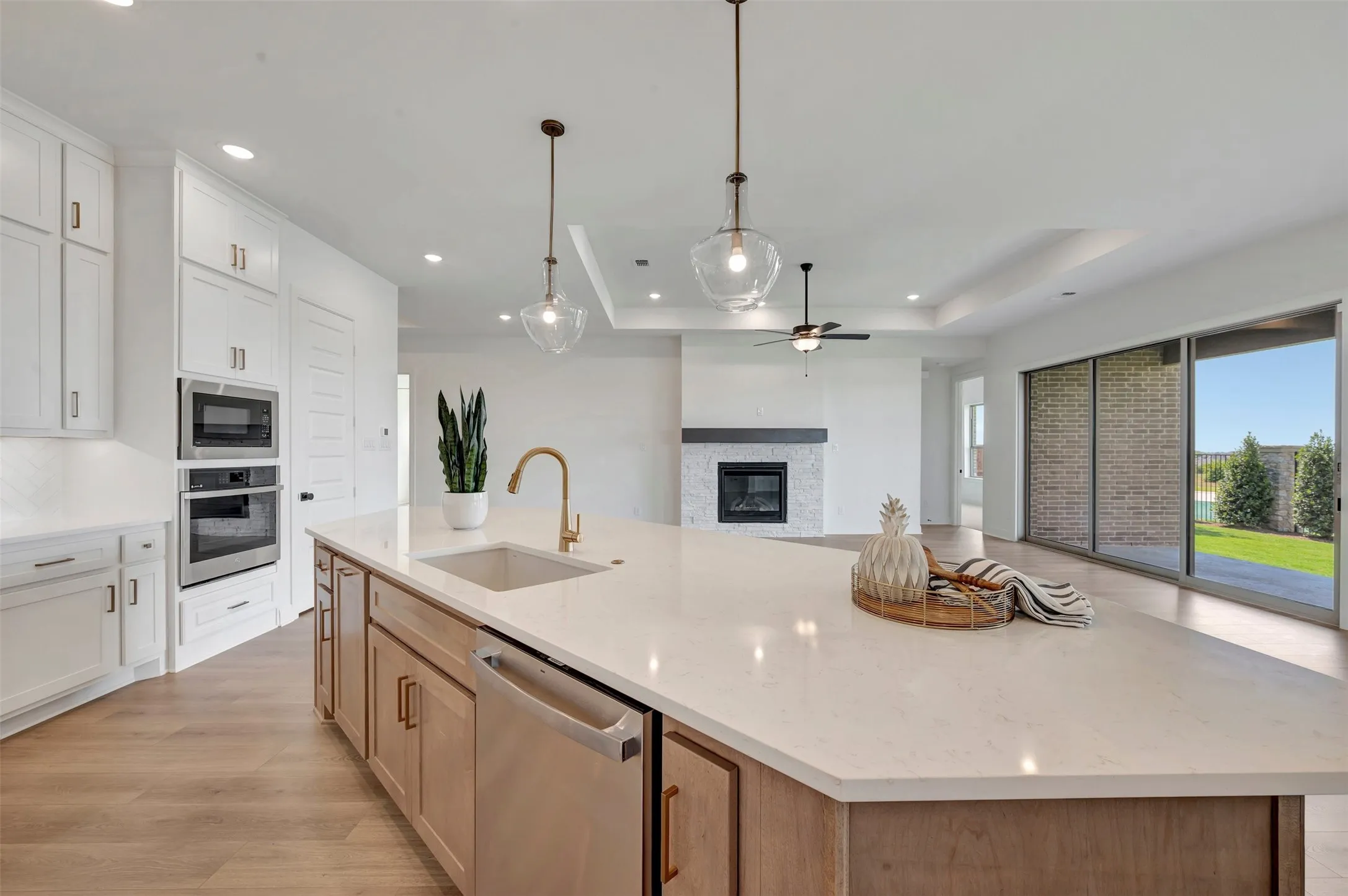 Chef's kitchen showcasing a large waterfall-edge island with wood-finish cabinetry, stainless steel appliances including dual wall ovens, quartz countertops, and a bronze gooseneck faucet