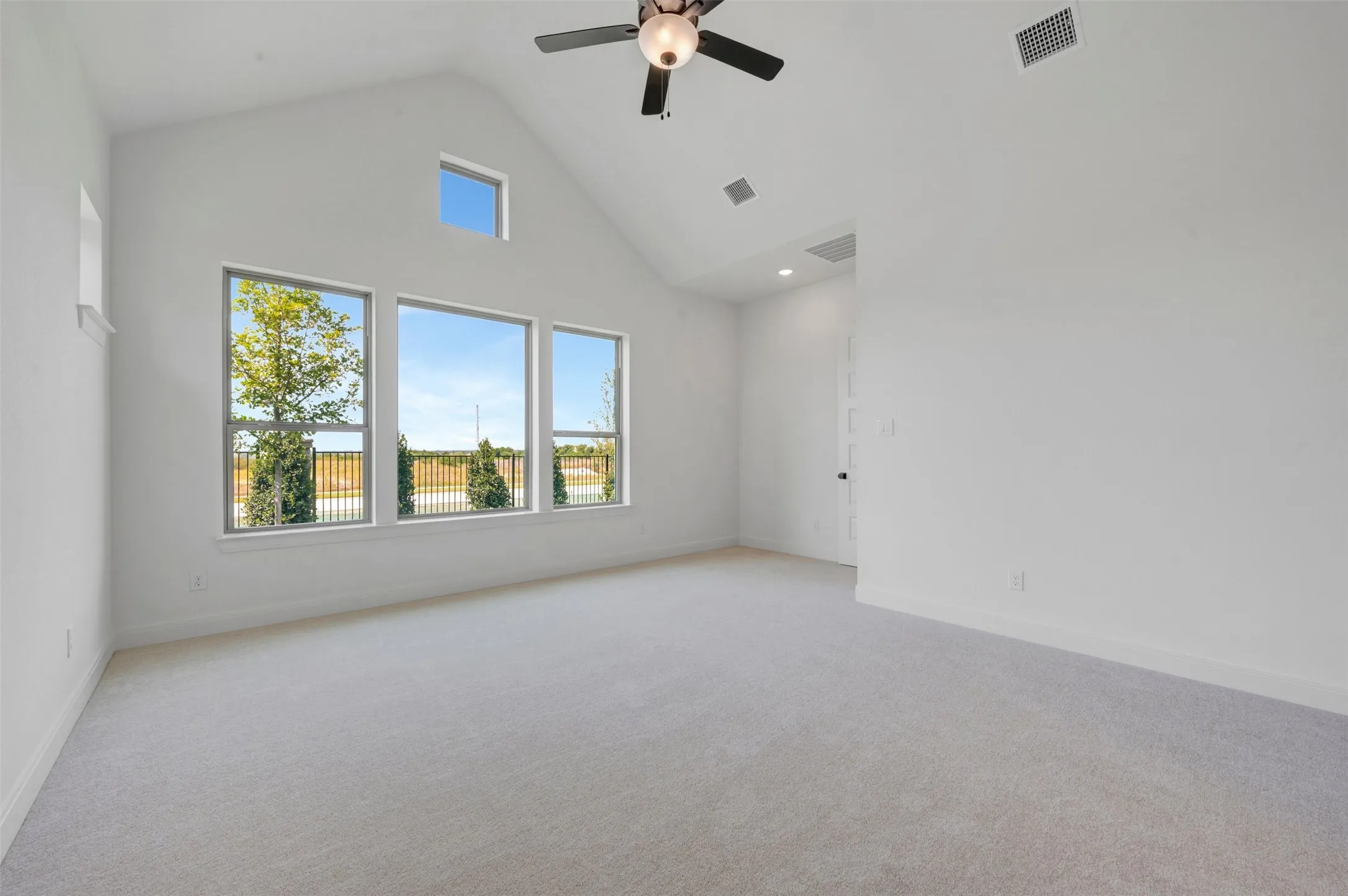 Bright and airy bedroom featuring abundant natural light from three expansive windows, neutral carpet flooring, cathedral ceiling with ceiling fan, and recessed lighting throughout