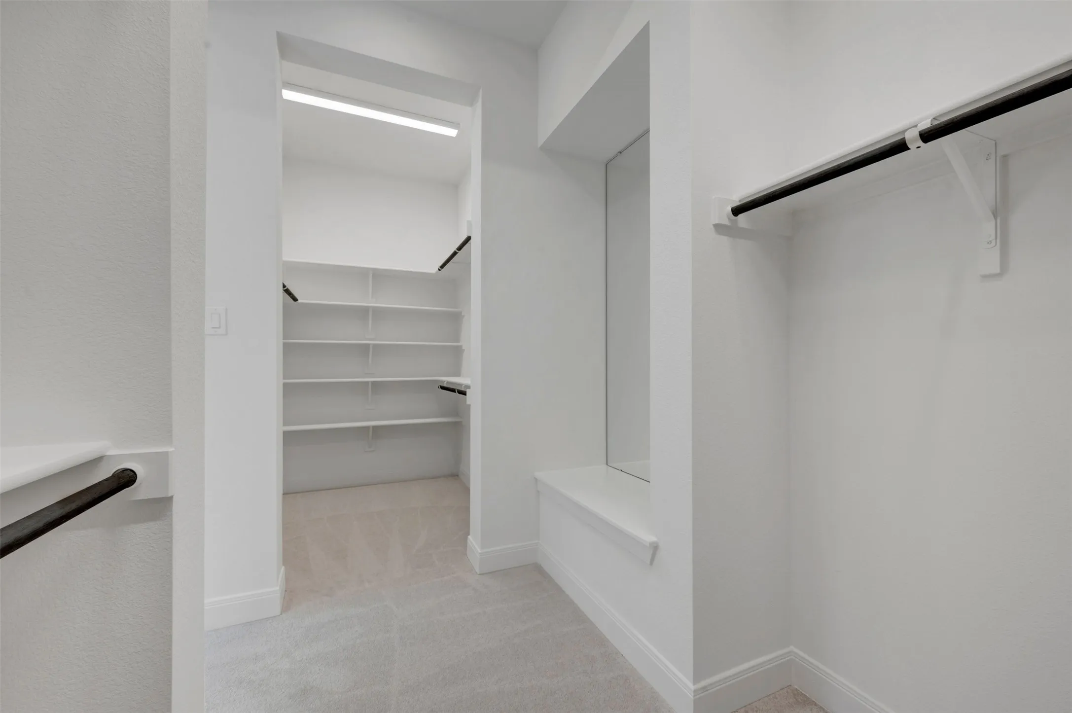 Spacious walk-in closet featuring multiple shelves for organized storage, polished concrete flooring, bright overhead lighting, and black metal hanging rods for garment display