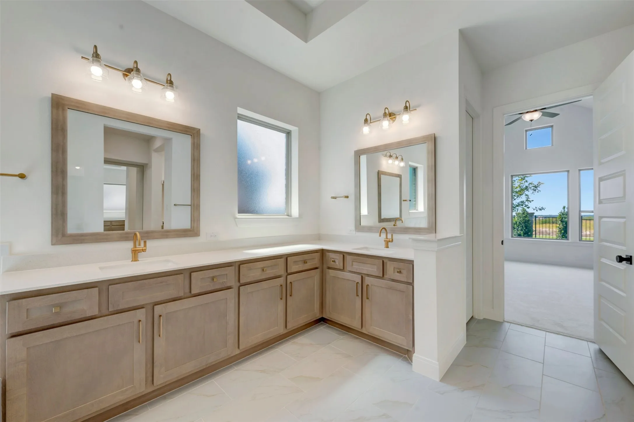 Spa-inspired primary bathroom featuring an expansive dual-sink vanity with wood-finish cabinetry, white quartz countertops, and brass-finish fixtures