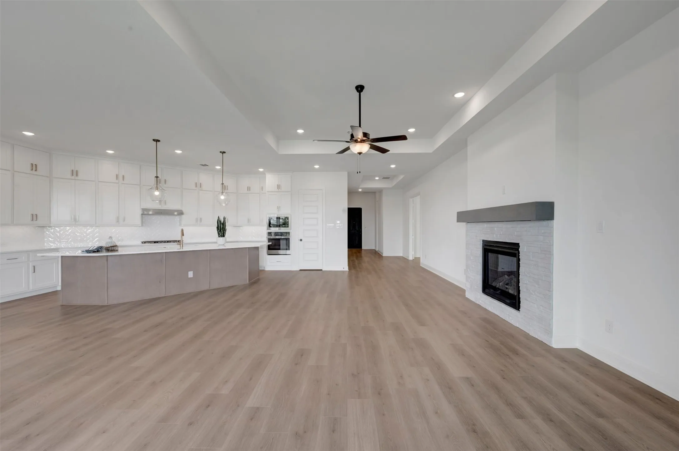 Spacious open-concept living area featuring wood-finish flooring, a contemporary fireplace with a stone surround, and an expansive kitchen island with pendant lighting