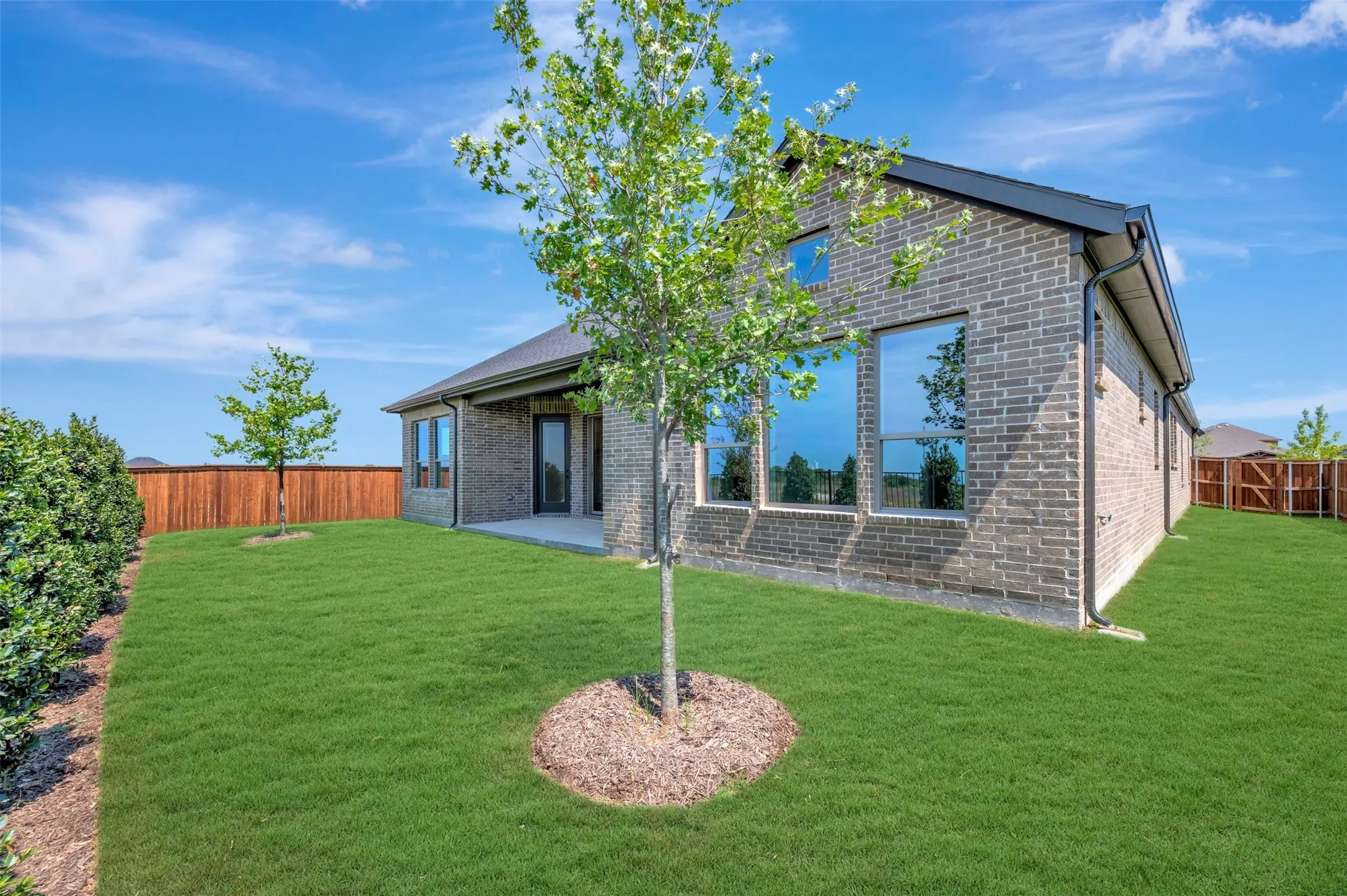 Expansive green lawn, brick exterior, large windows, covered patio, and wooden privacy fencing