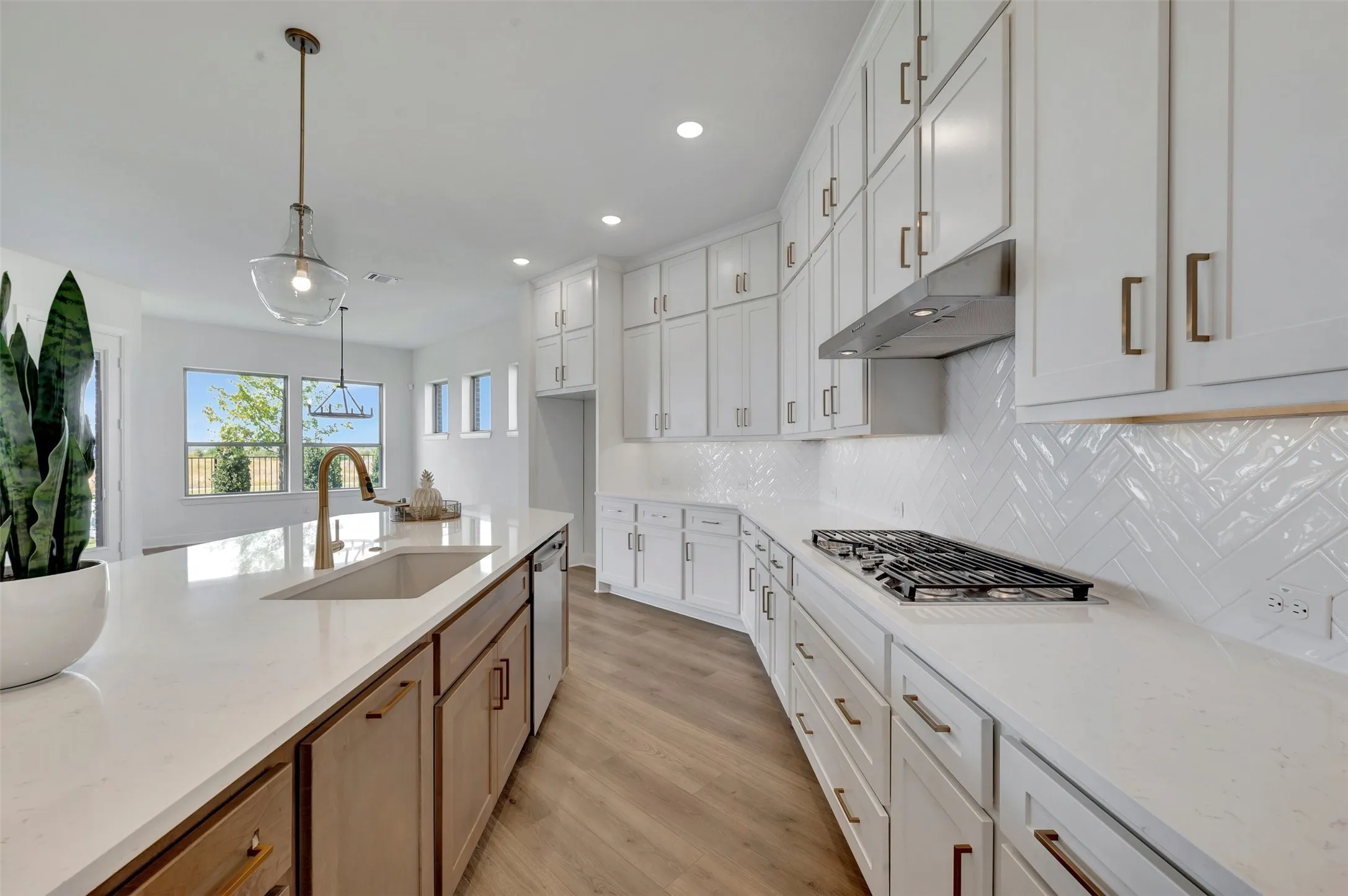 Chef's kitchen featuring white cabinetry with brushed bronze hardware, white subway tile backsplash in herringbone pattern, gas cooktop, stainless steel appliances, white quartz countertops, and a large center island with wood-finish base